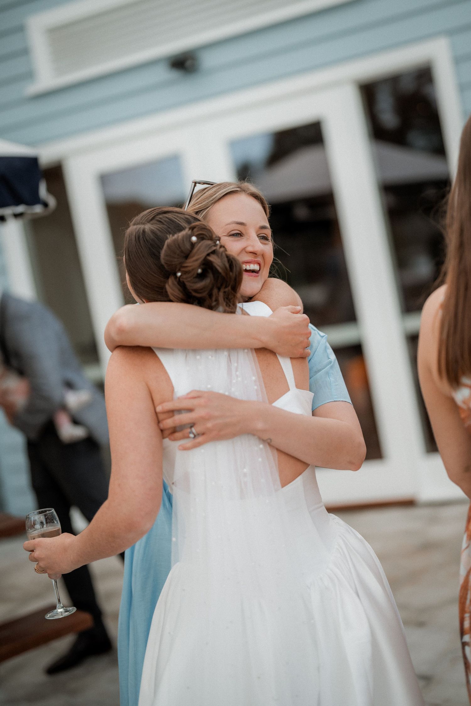 Bridesmaids in light blue dresses share emotional hugs with the bride at an elegant outdoor venue.