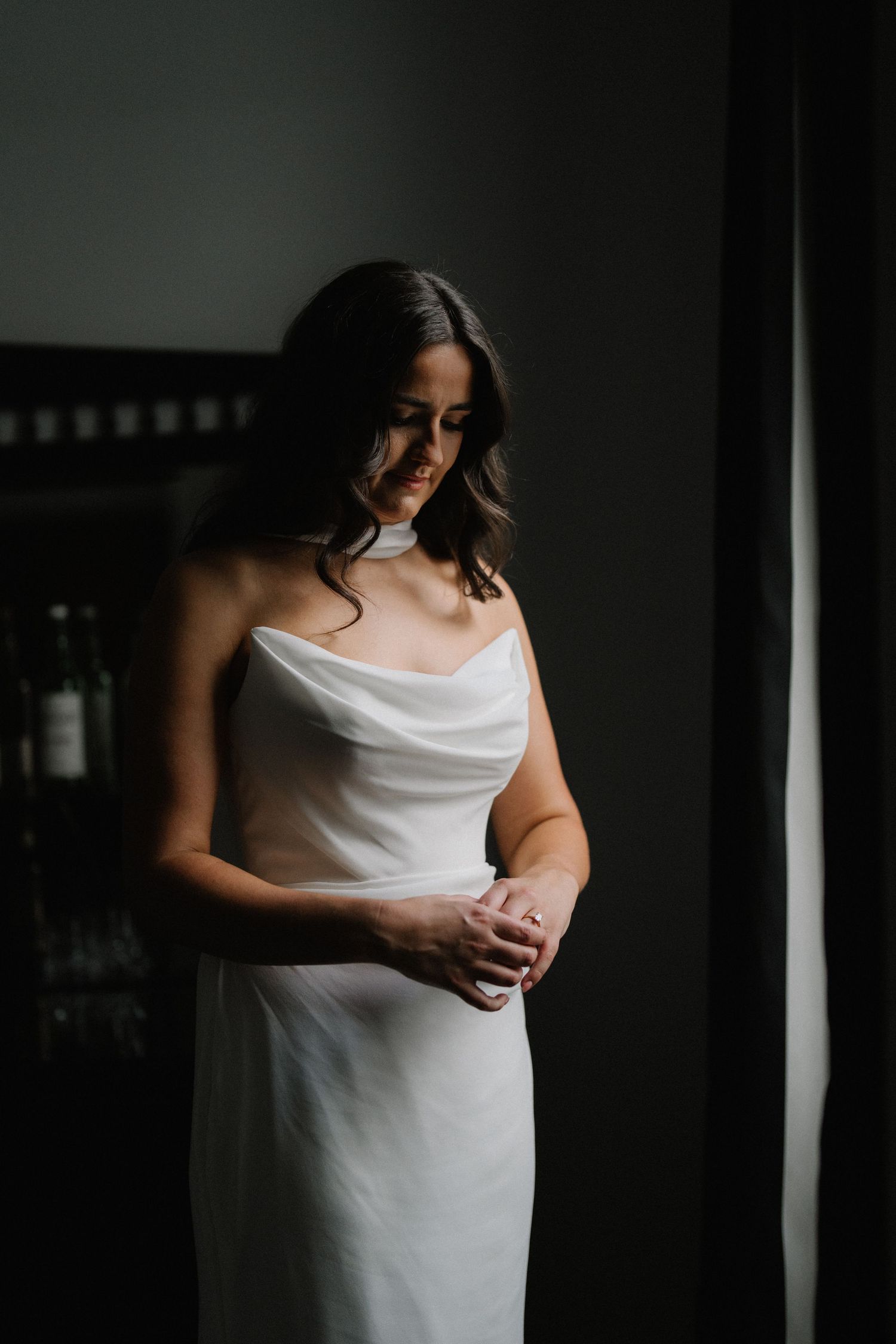 Artistic bridal portrait series showing elegant white dress details in moody window lighting.