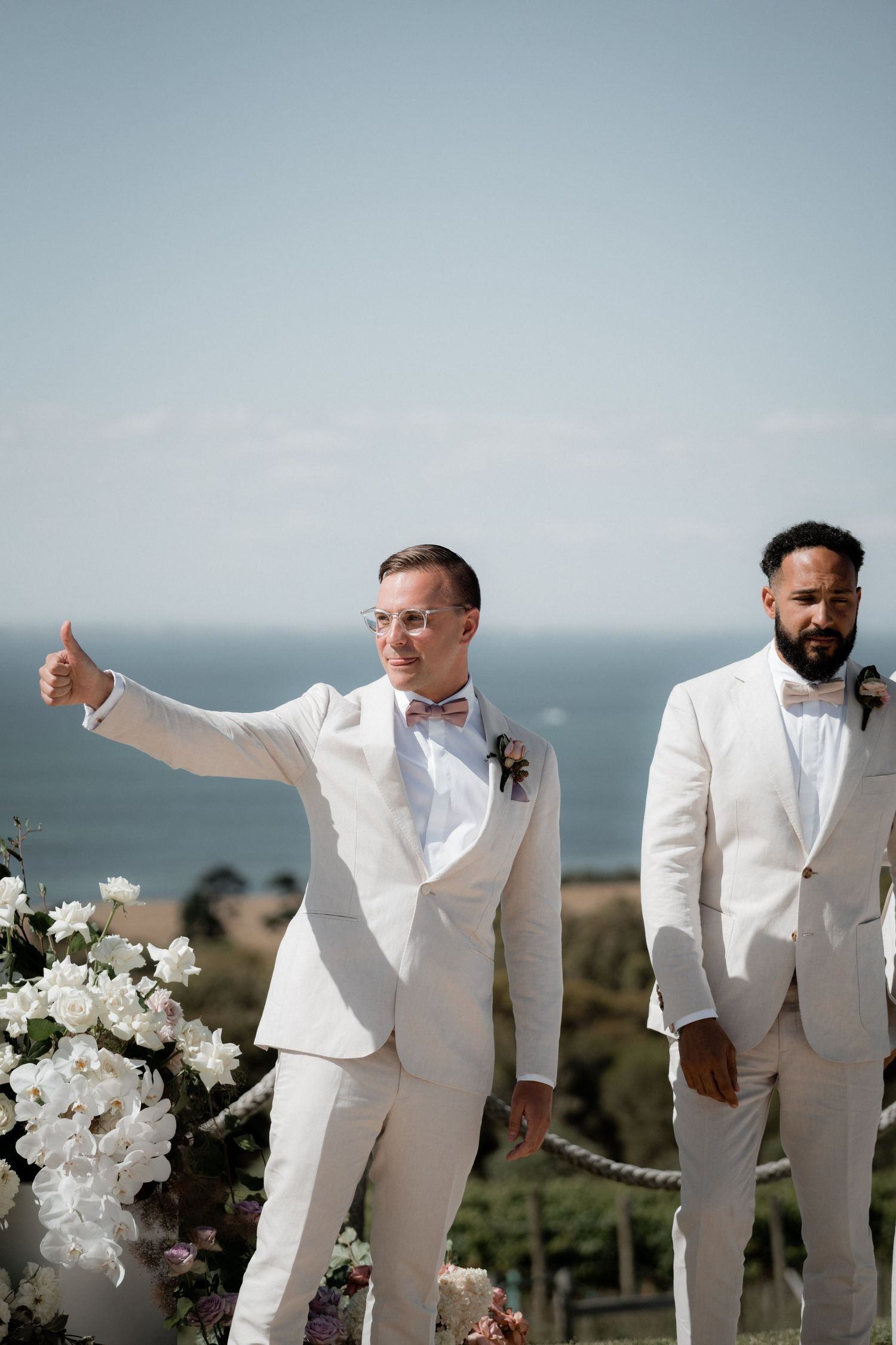 Groomsmen in crisp white suits pose together against a scenic coastal backdrop.