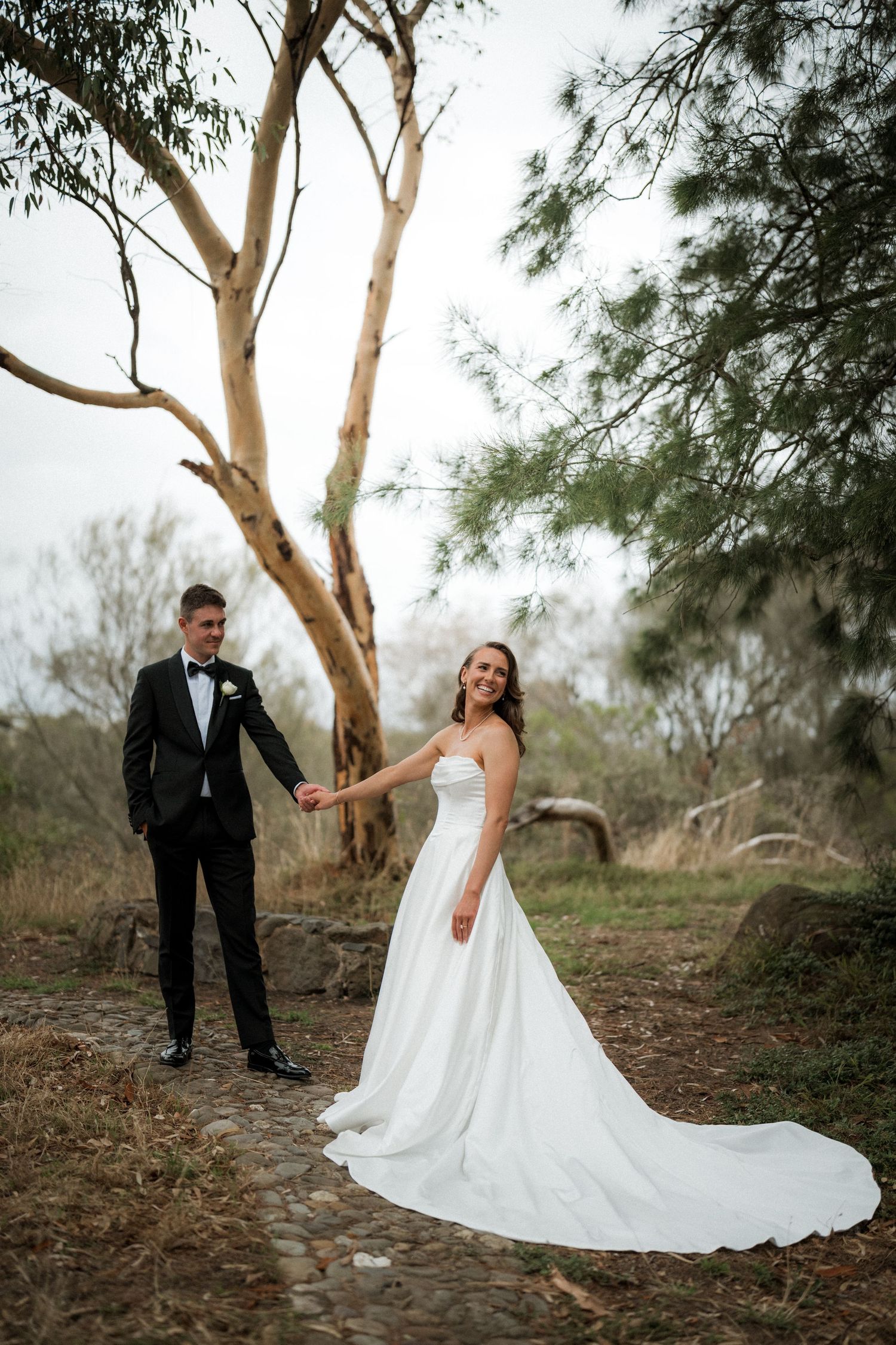 Wedding couple poses playfully among eucalyptus trees in natural outdoor setting.
