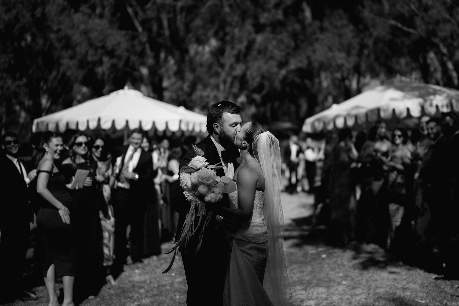 Bride and groom share a romantic kiss while walking down the aisle at an outdoor wedding ceremony.