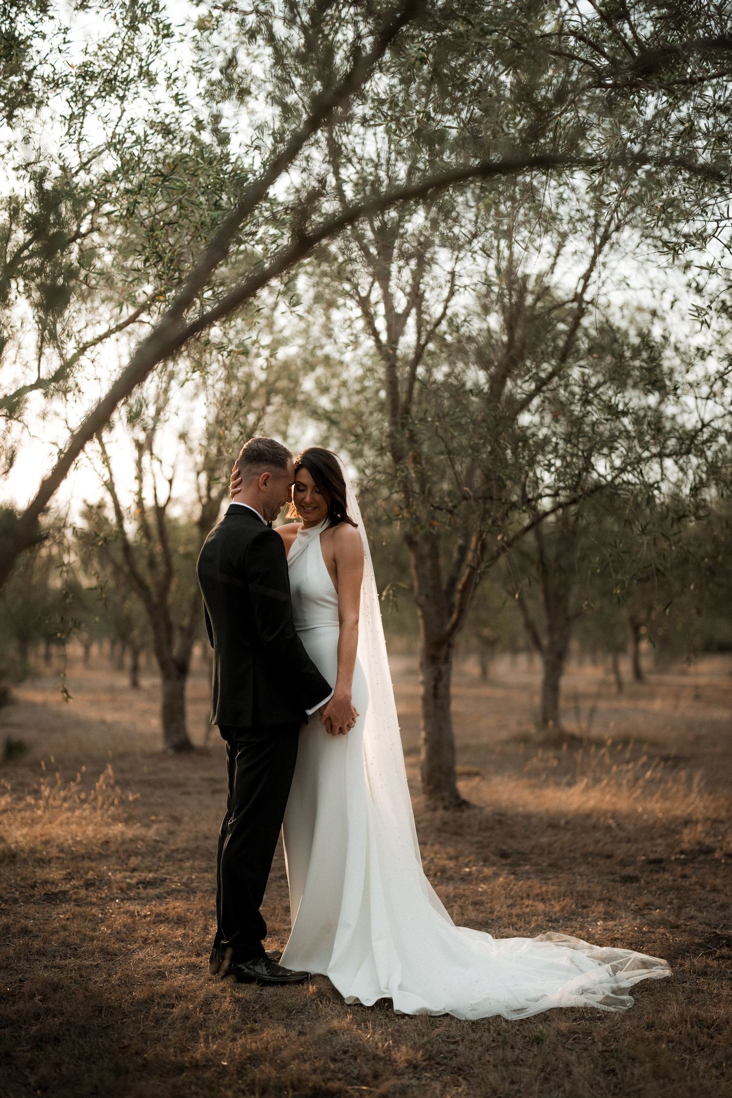 Romantic newlyweds share an intimate moment in a rustic outdoor setting at golden hour.
