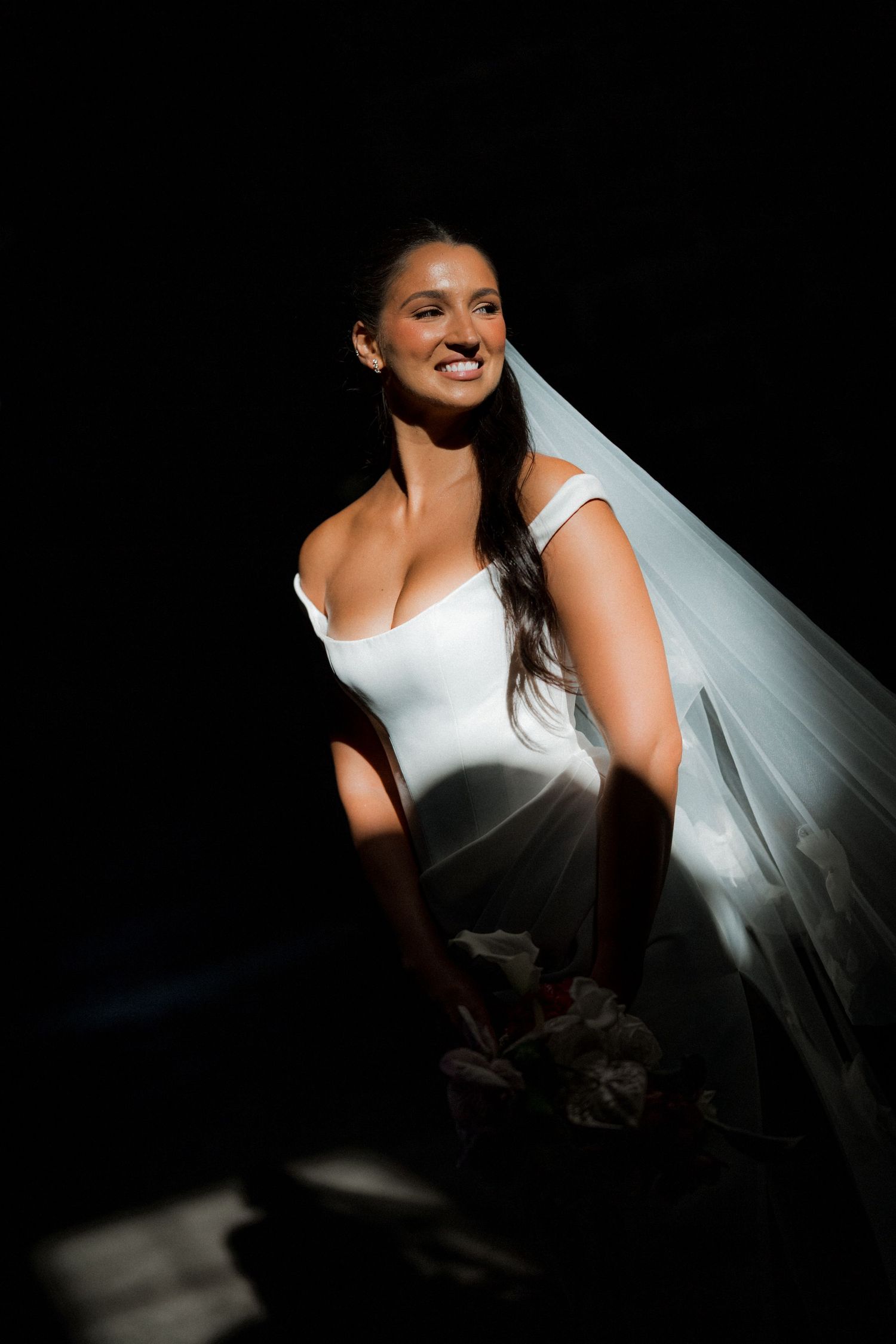 Artistic bridal portrait with dramatic side lighting against dark background.