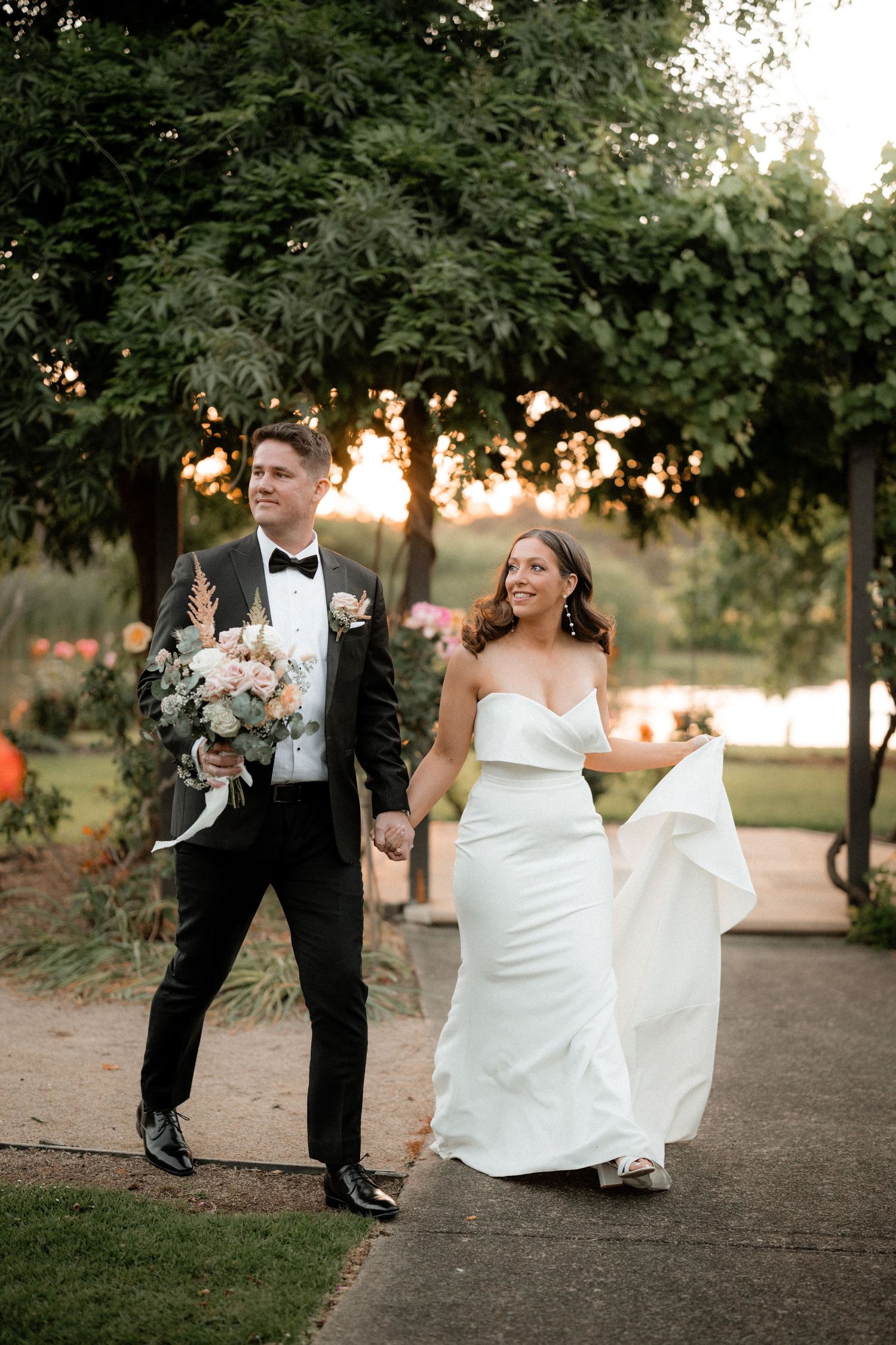 Couple dances and spins together on a tree-lined path at sunset.