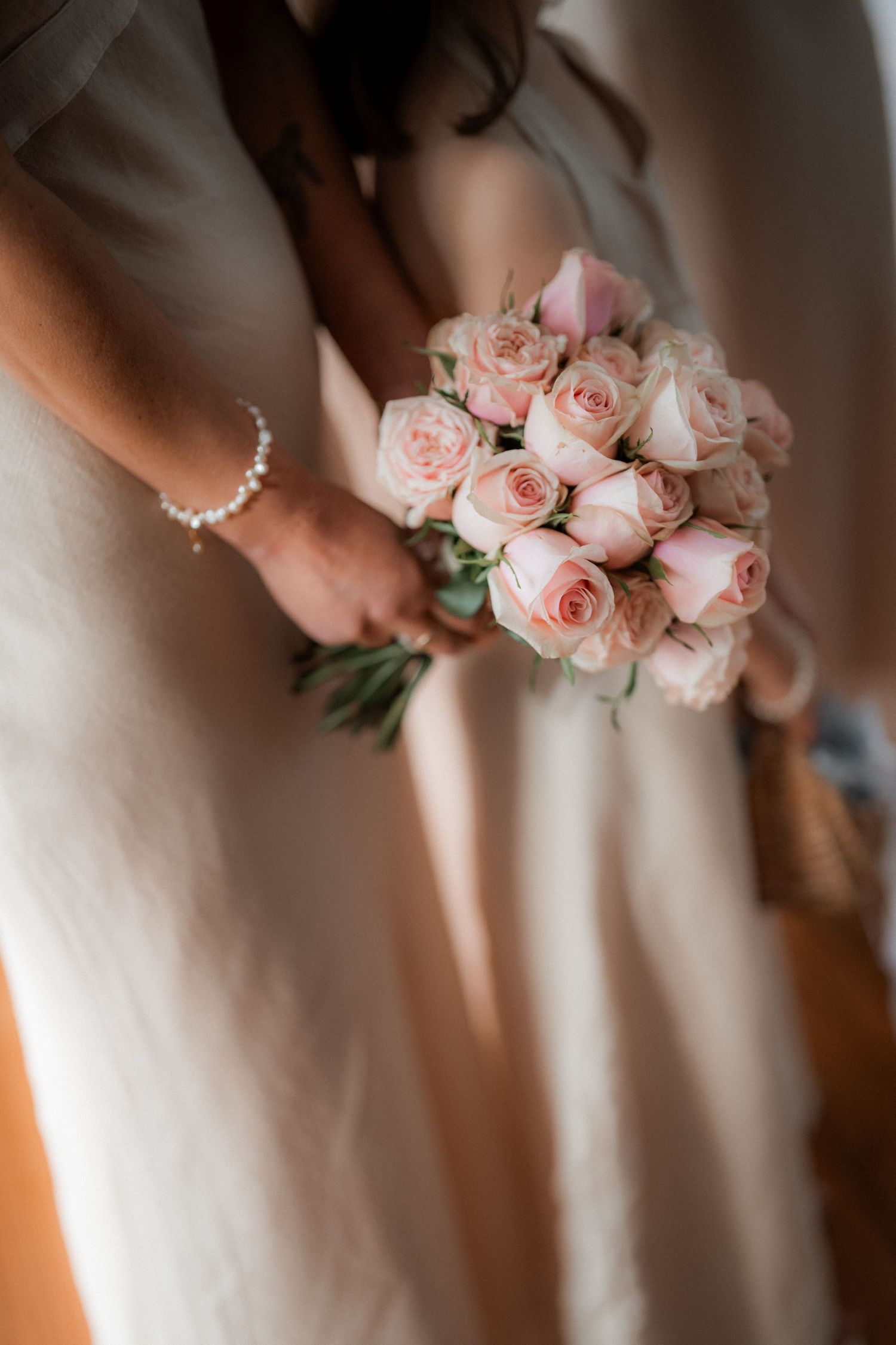 Delicate pink roses held against white fabric create soft wedding detail shot.