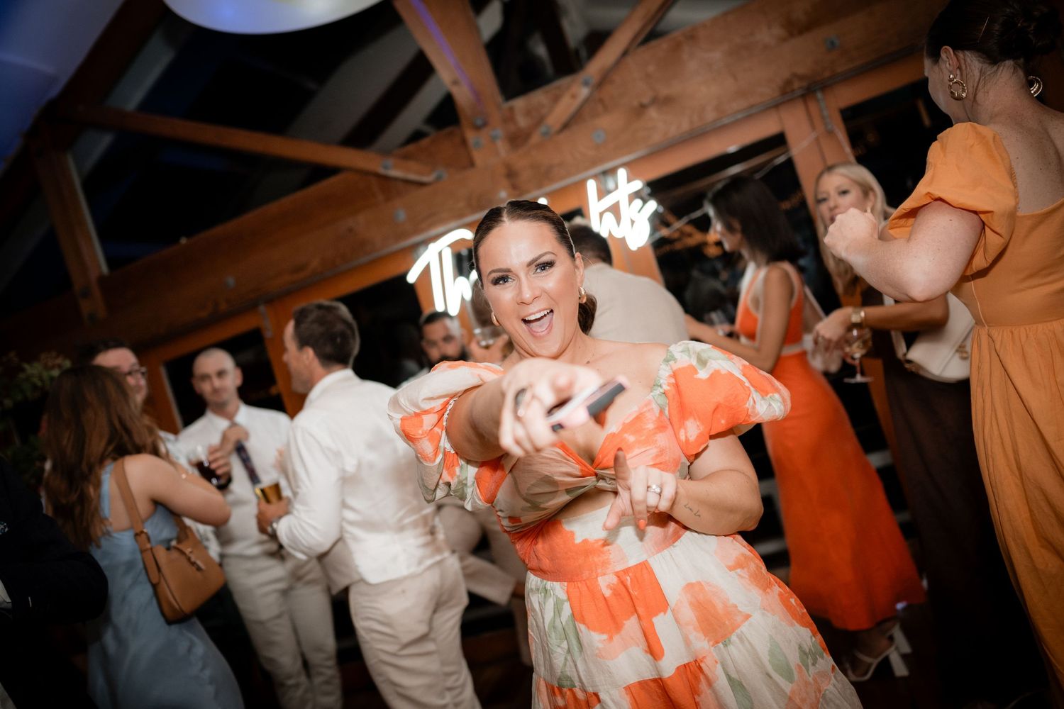 Wedding reception dance party with guests in coral and white attire celebrating on wooden dance floor.