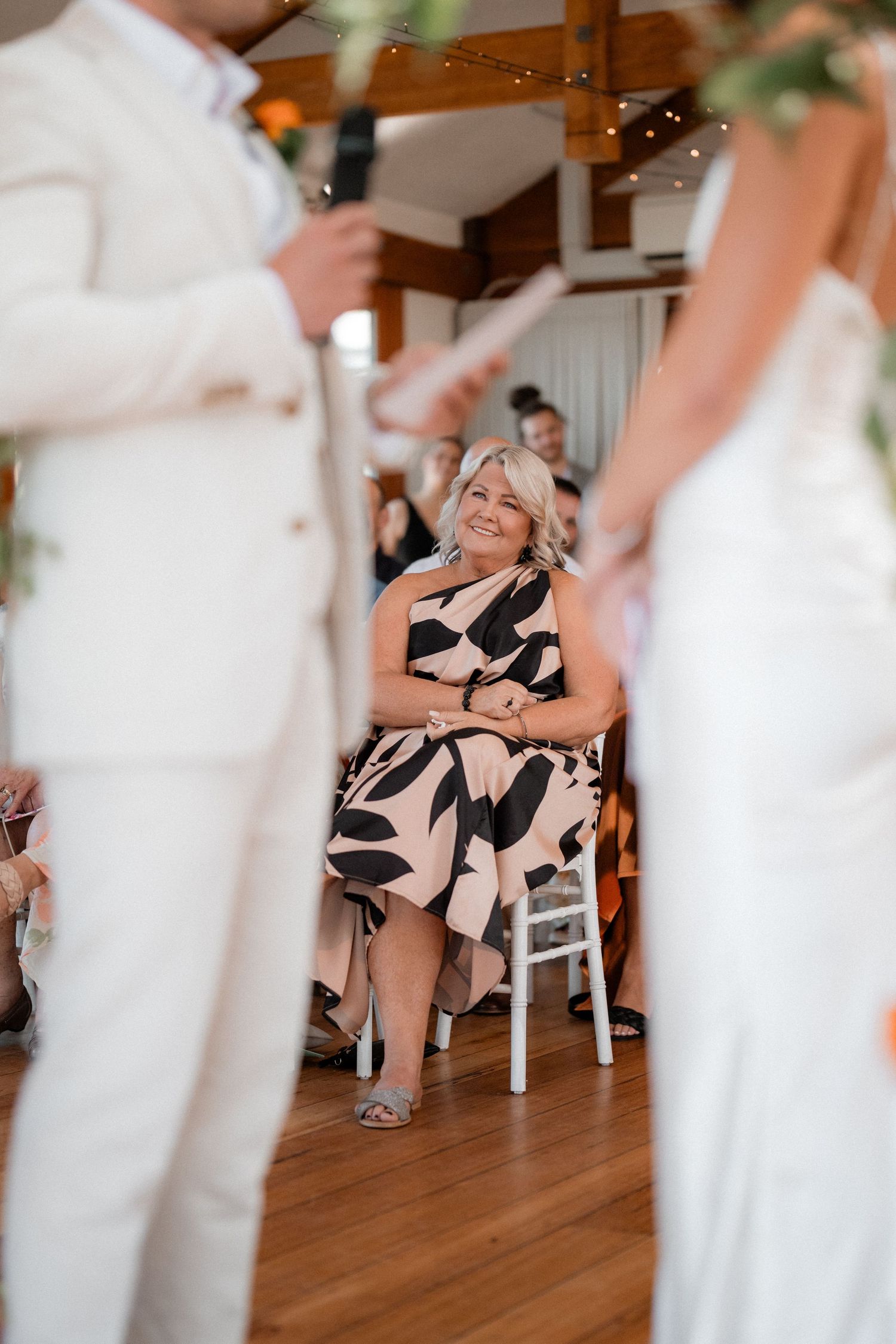 Wedding guests seated in white chairs during indoor reception.