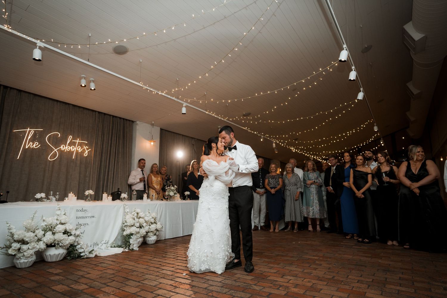 Wedding reception venue decorated with string lights and a dance floor surrounded by guests.