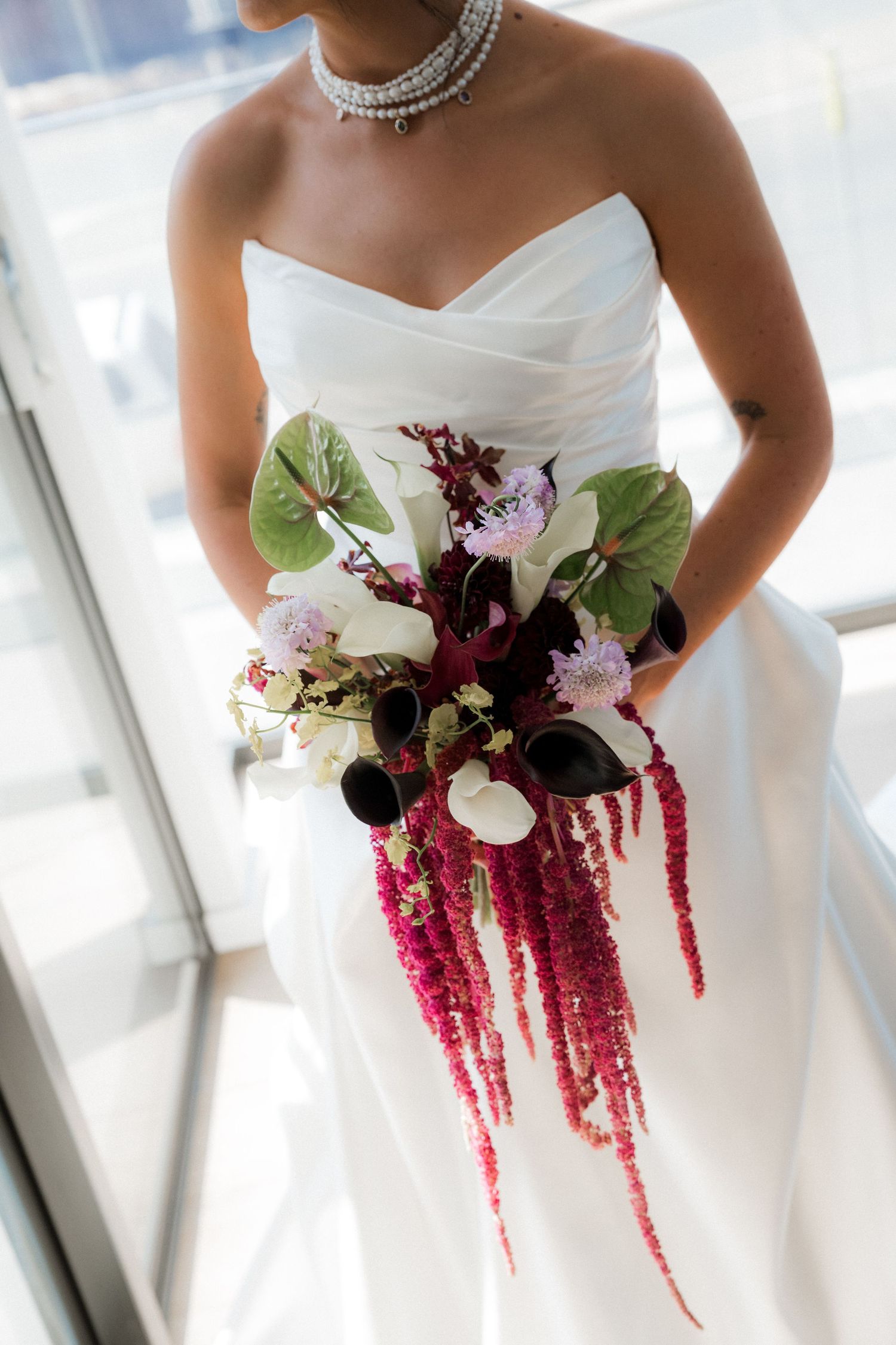 Elegant bridal bouquet features dramatic burgundy amaranthus and white flowers against a white wedding gown.
