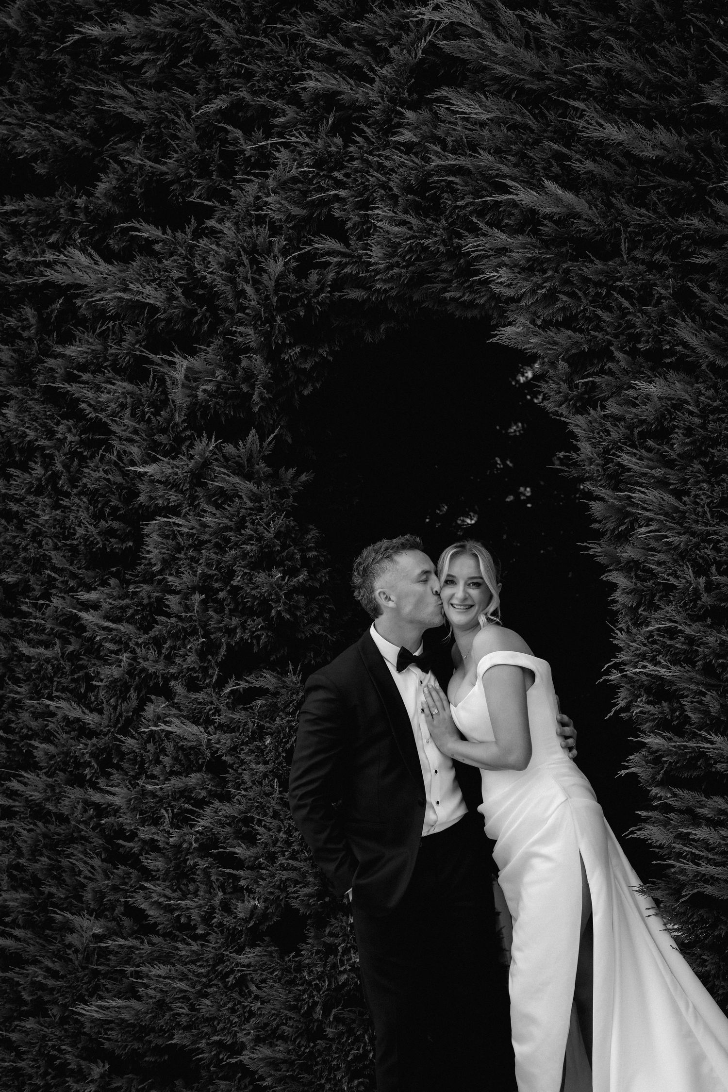 Intimate black and white portrait against a dark hedge background.