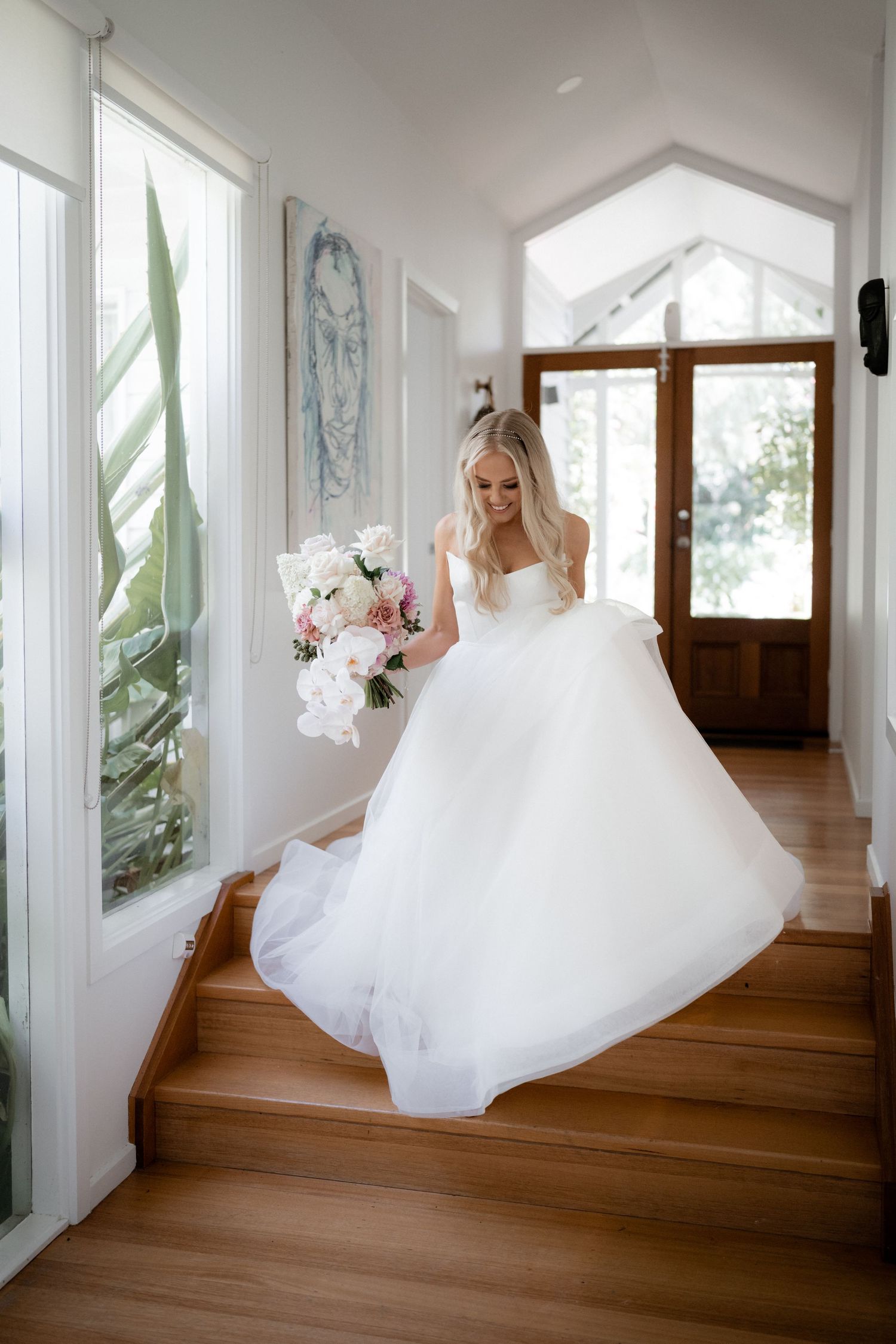 A billowing white wedding gown flows through a bright hallway with hardwood flooring.