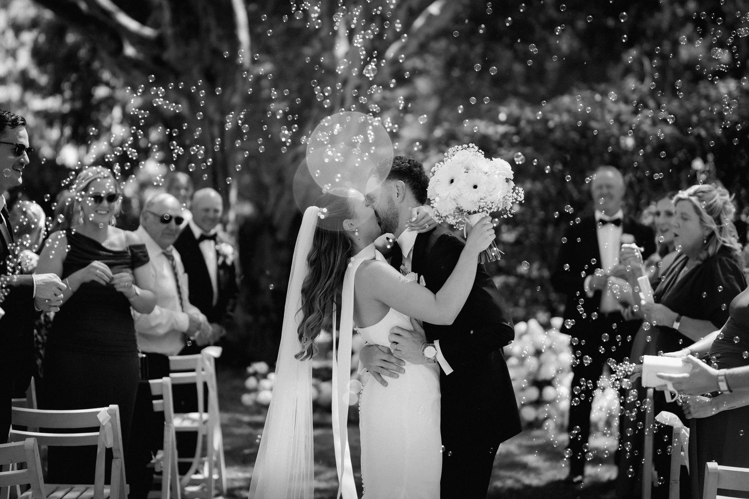 Wedding celebration with guests throwing confetti during an outdoor garden ceremony.