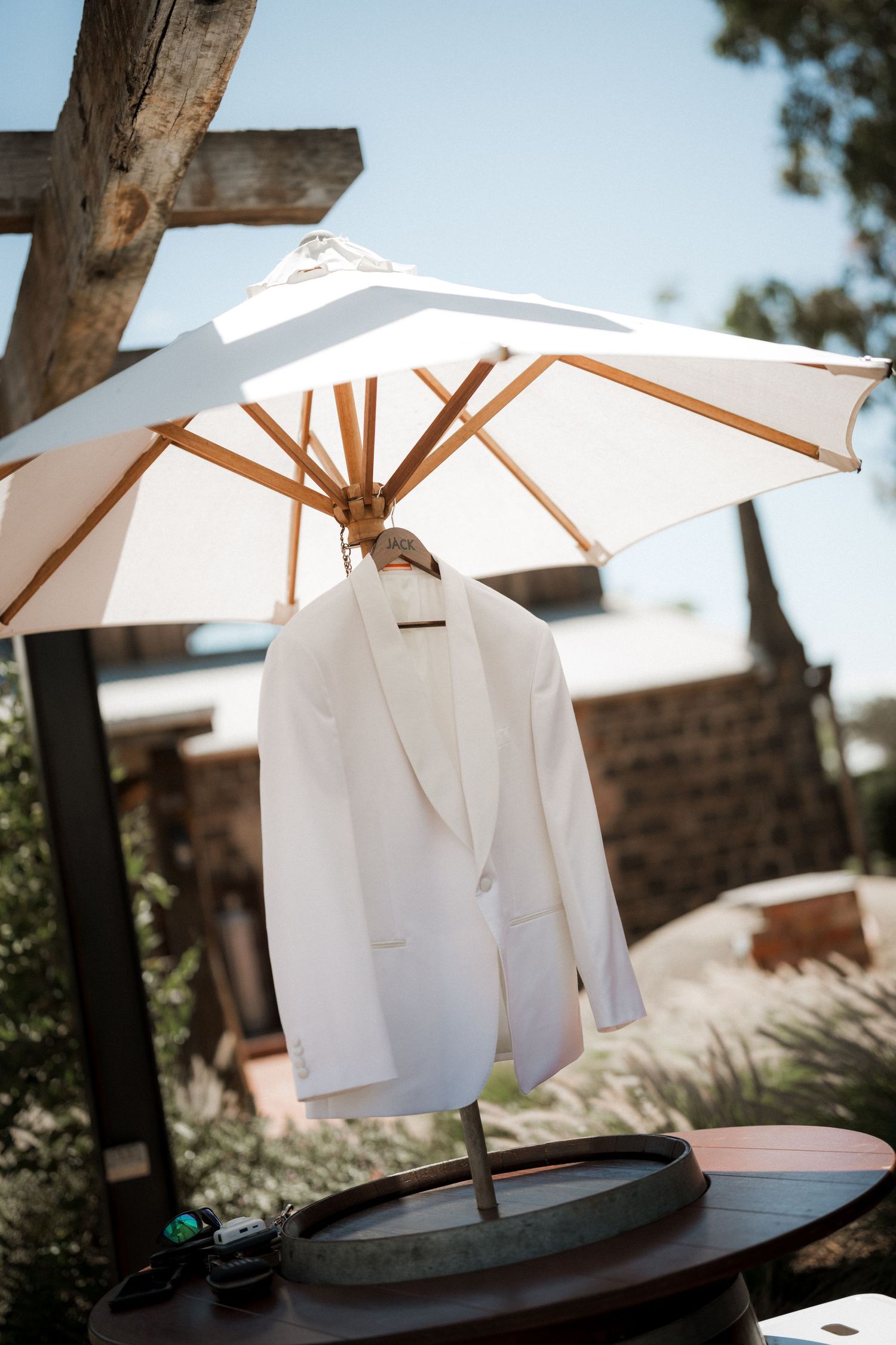 White tuxedo jacket hanging from outdoor patio umbrella in sunny garden setting.