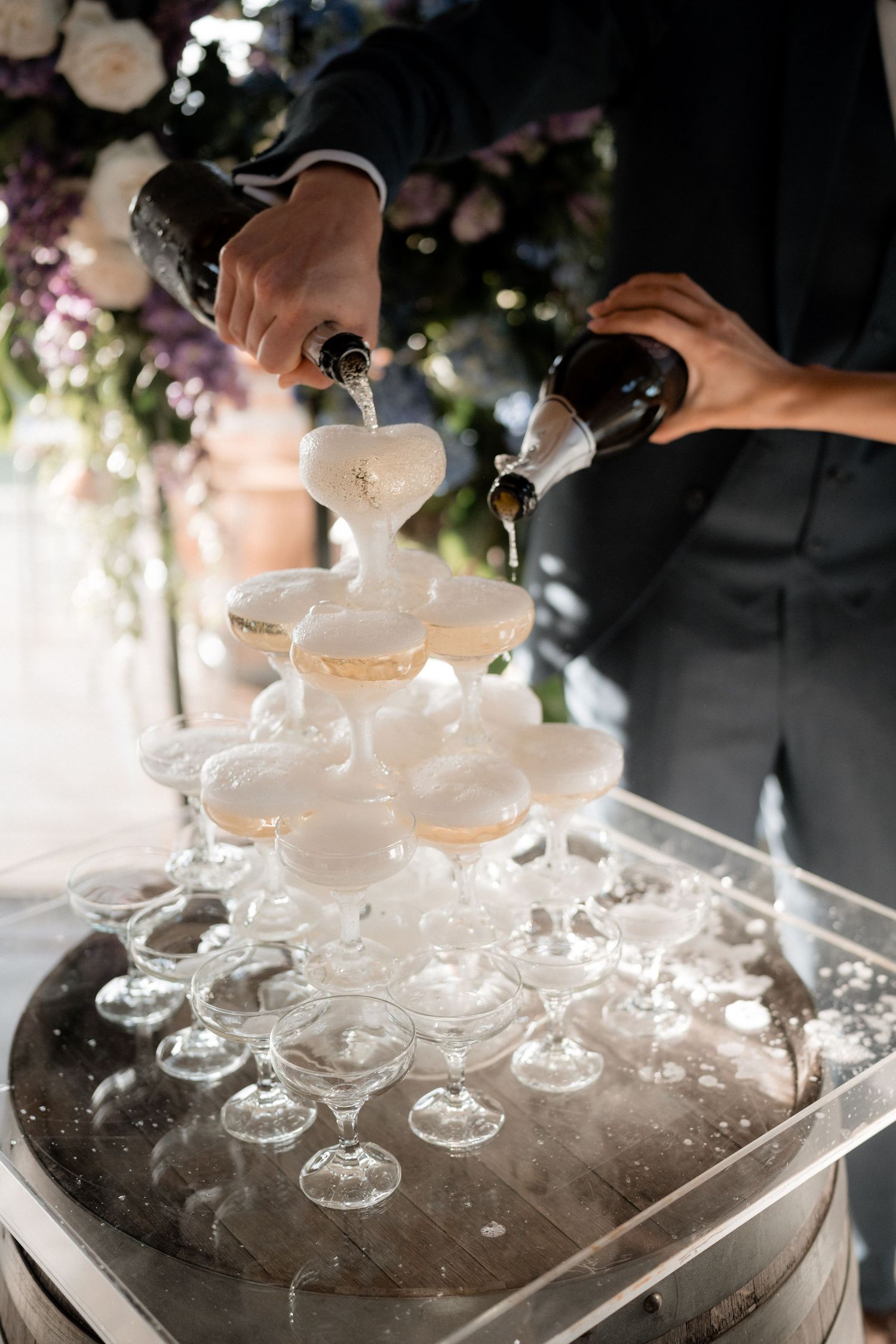 Champagne being poured into a tower of elegant coupe glasses at a wedding celebration.