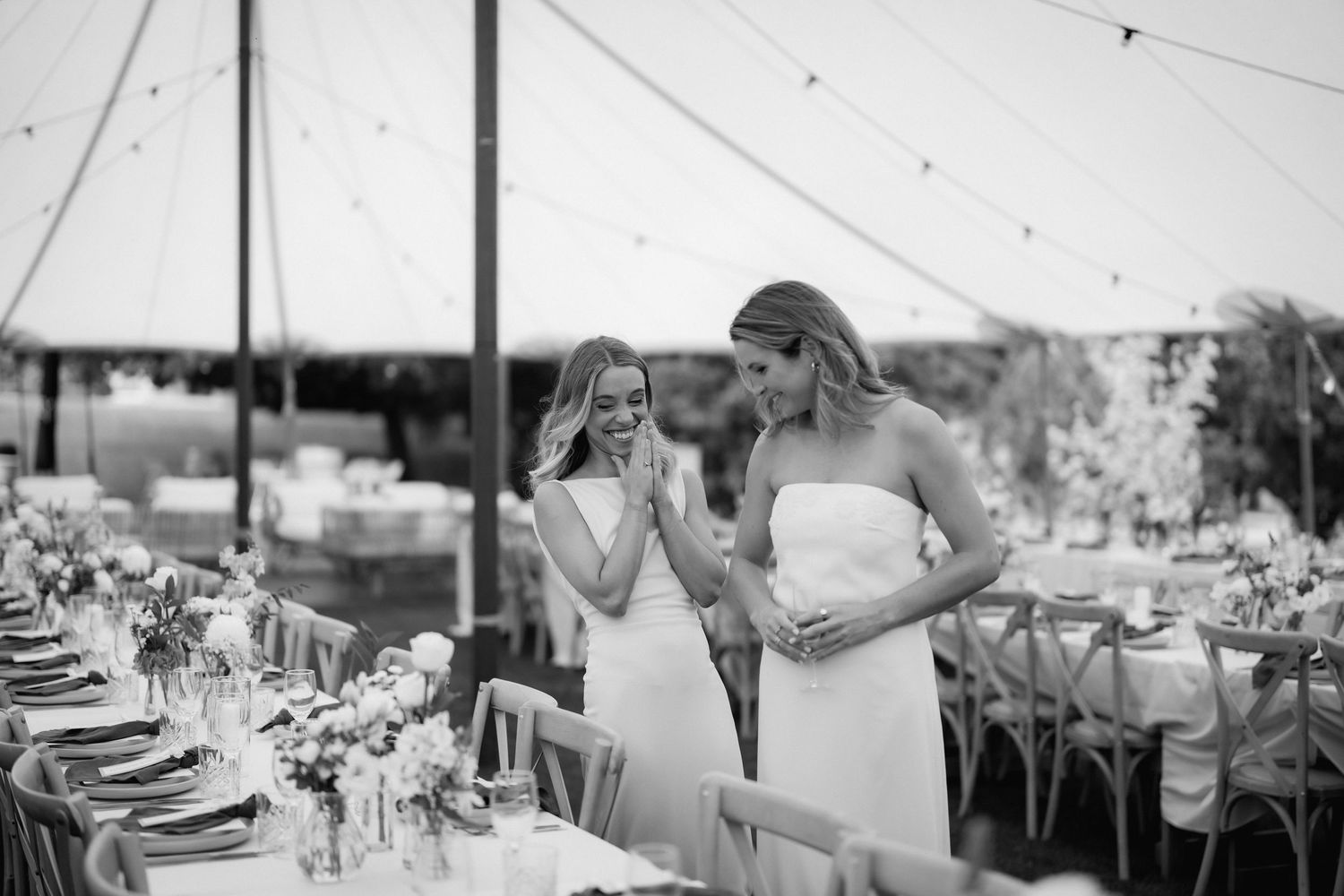 Two people stand together at an elegant outdoor reception with tables set for dining under a tent.
