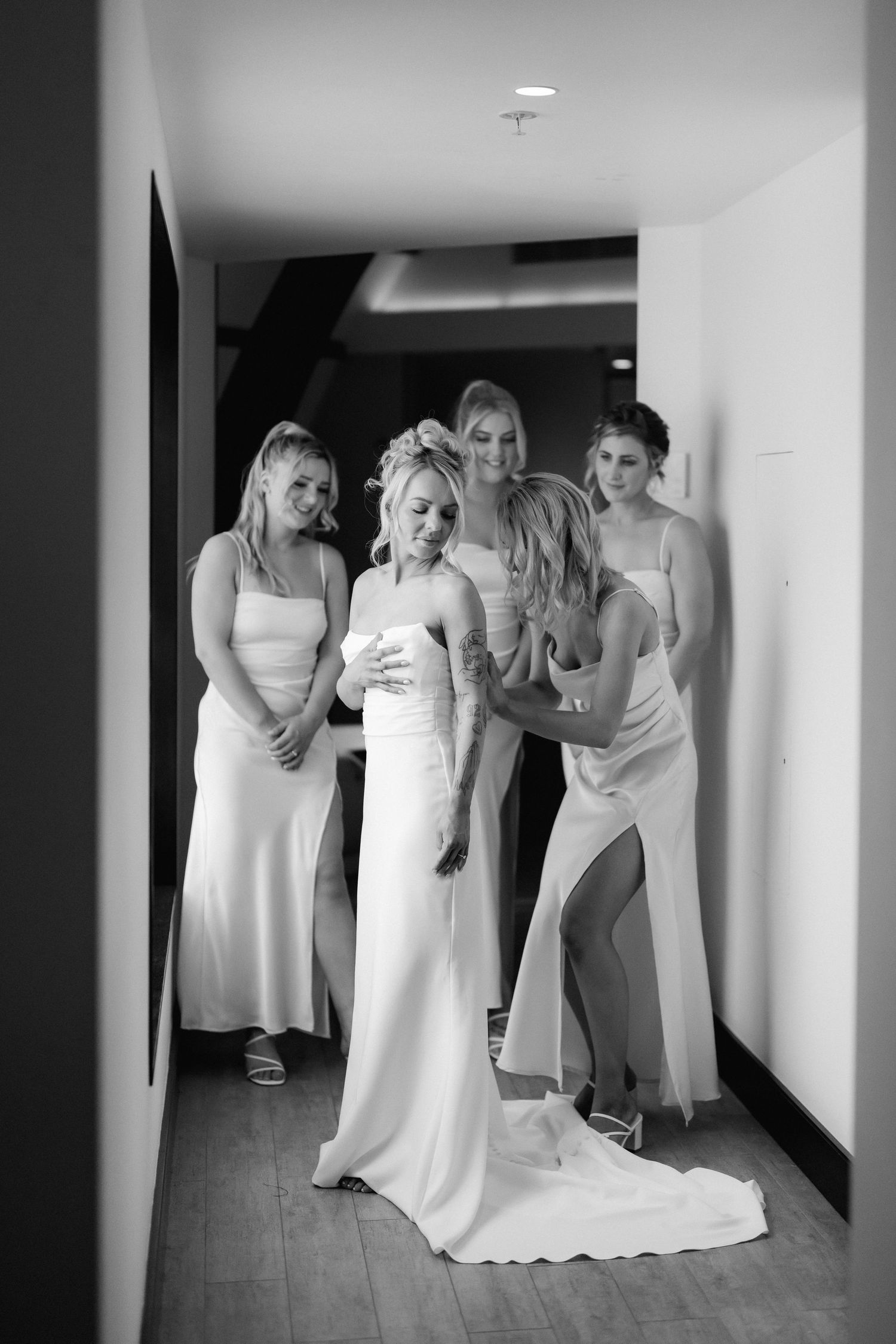 A candid moment of bridesmaids helping with wedding preparations in an indoor hallway.
