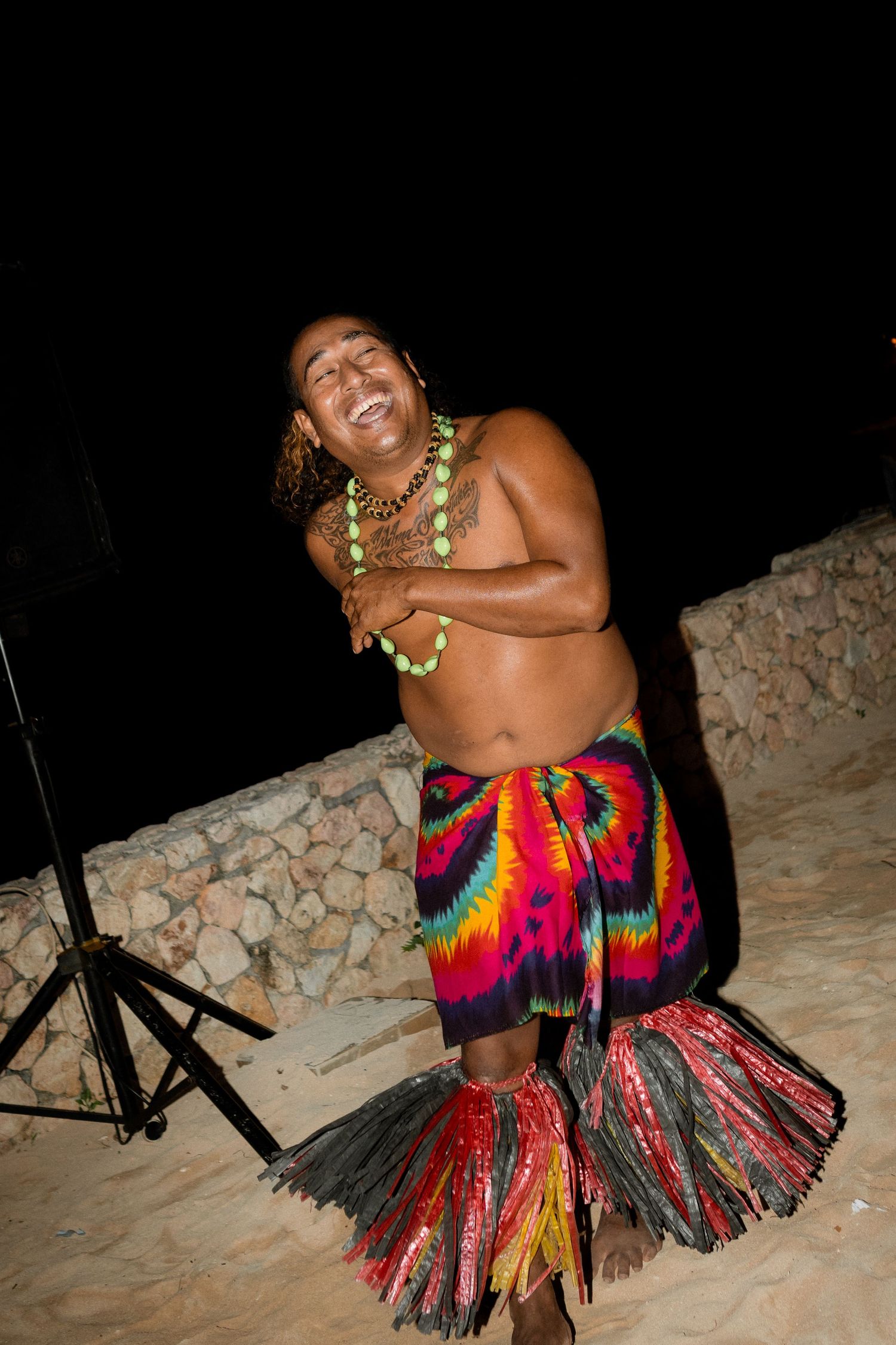 A traditional Hawaiian performer in a colorful grass skirt and lei performs at a beachside event.