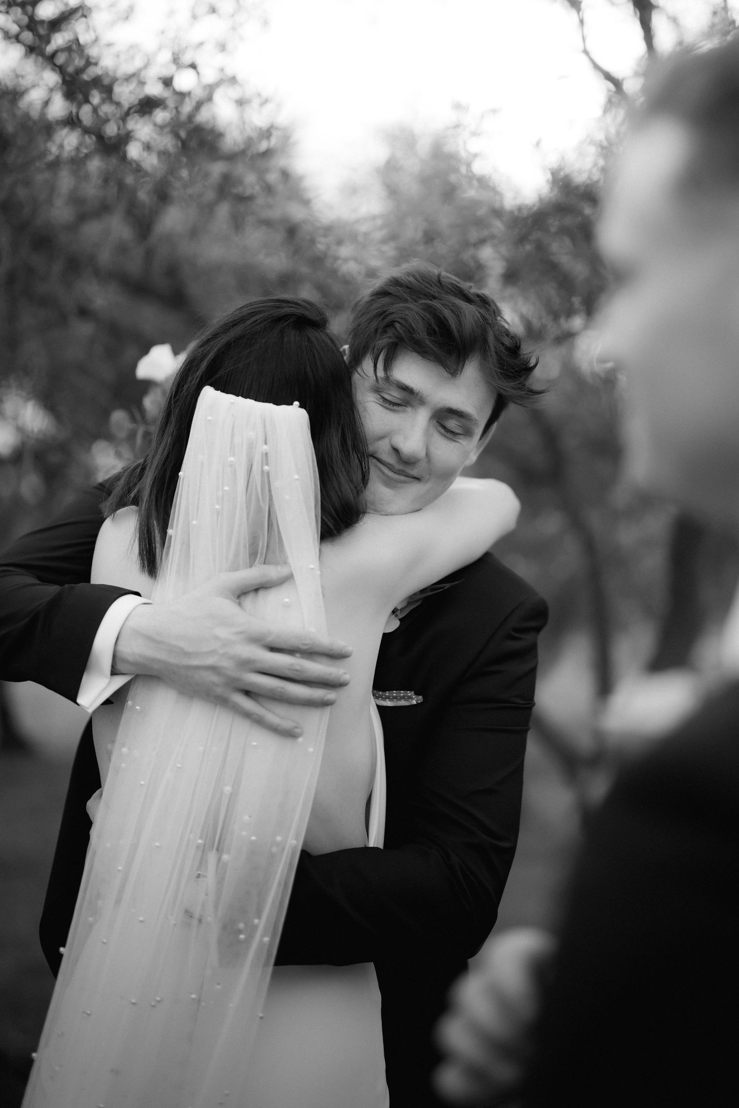 Emotional black and white wedding embrace captured during outdoor celebration.
