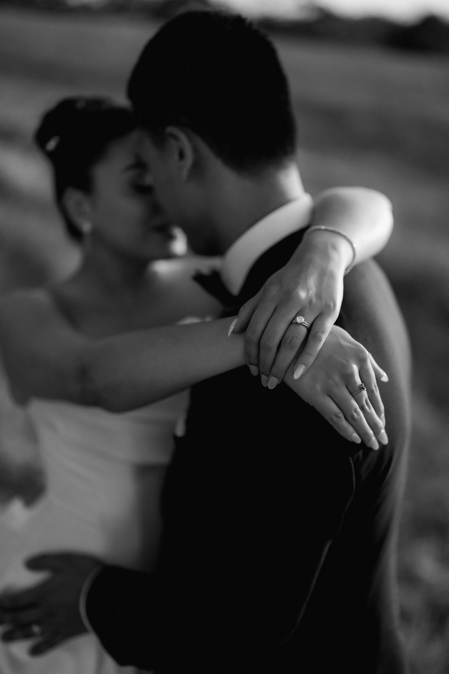 Black and white intimate portrait of newlyweds embracing with wedding ring visible.
