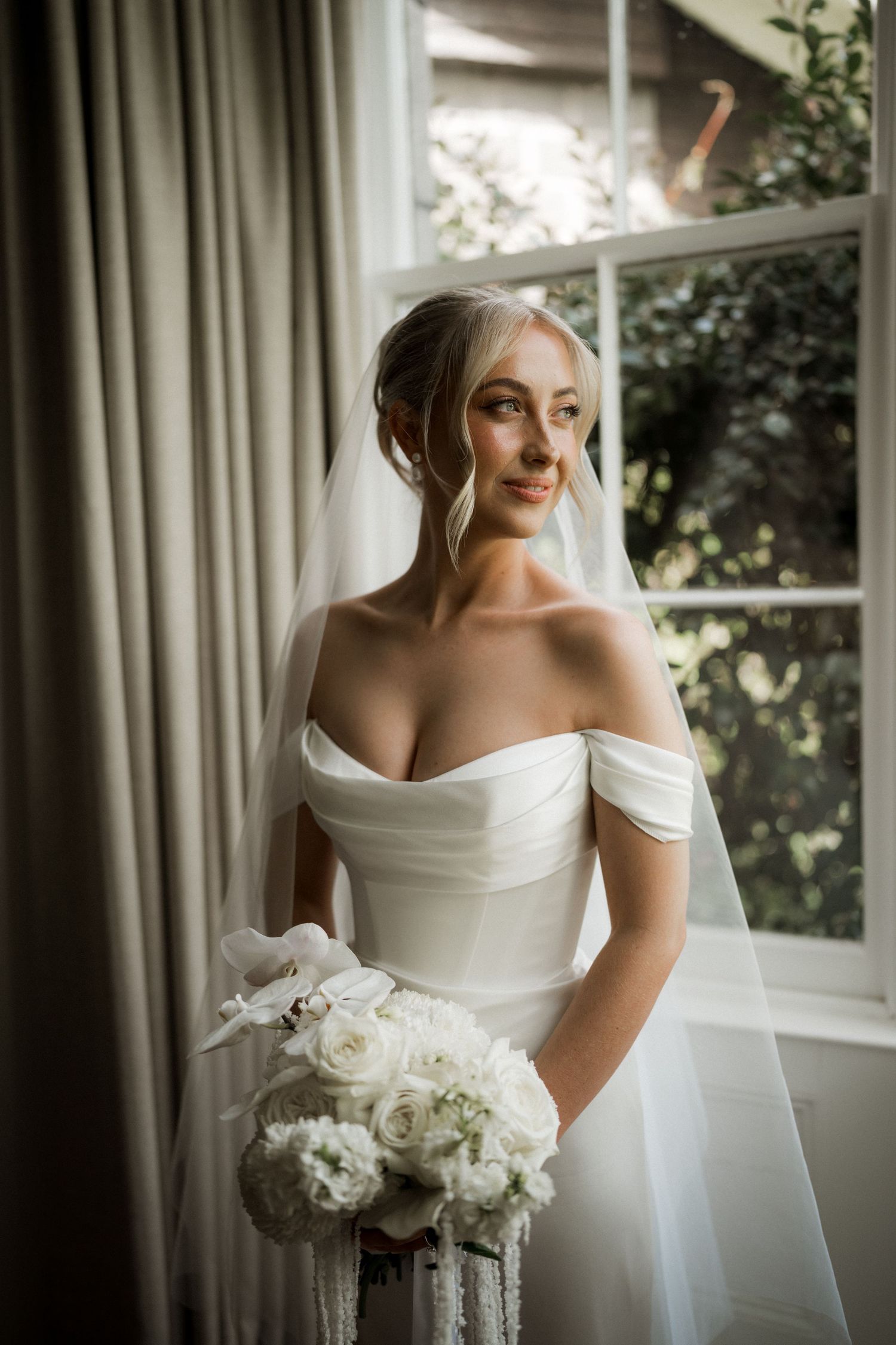 Elegant bridal portrait series showing a white off-shoulder wedding gown and classic white peony bouquet near sunlit windows.