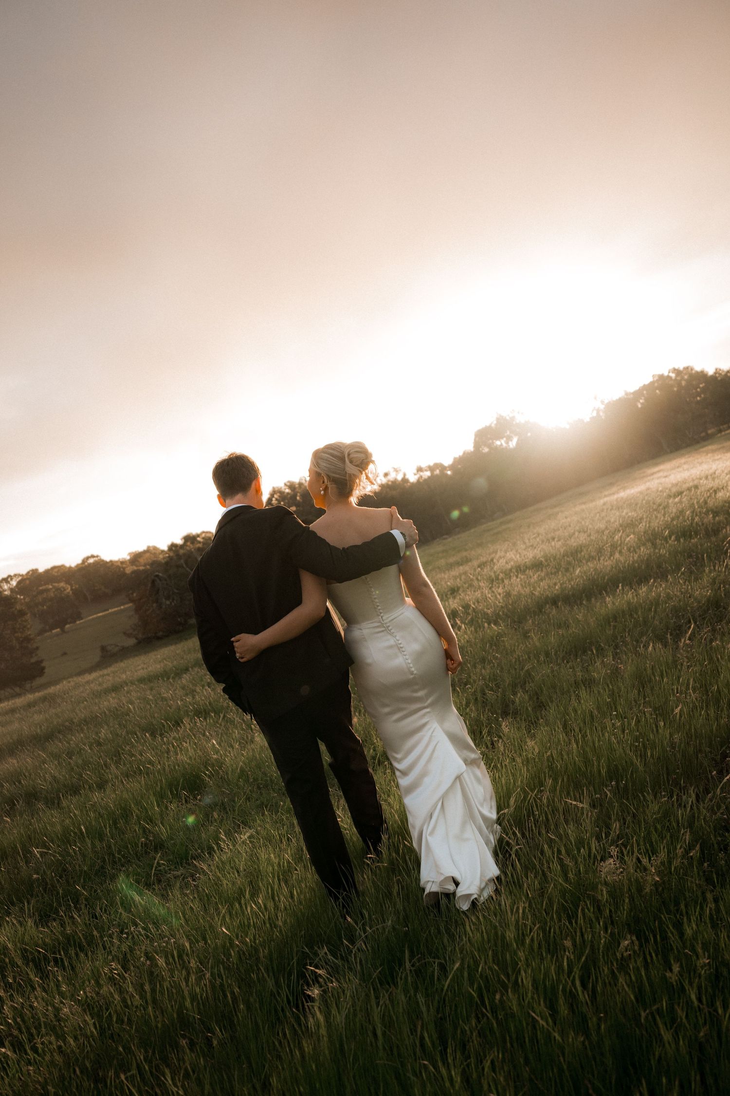 Couple embraces in a field during golden hour sunset creating a romantic silhouette.
