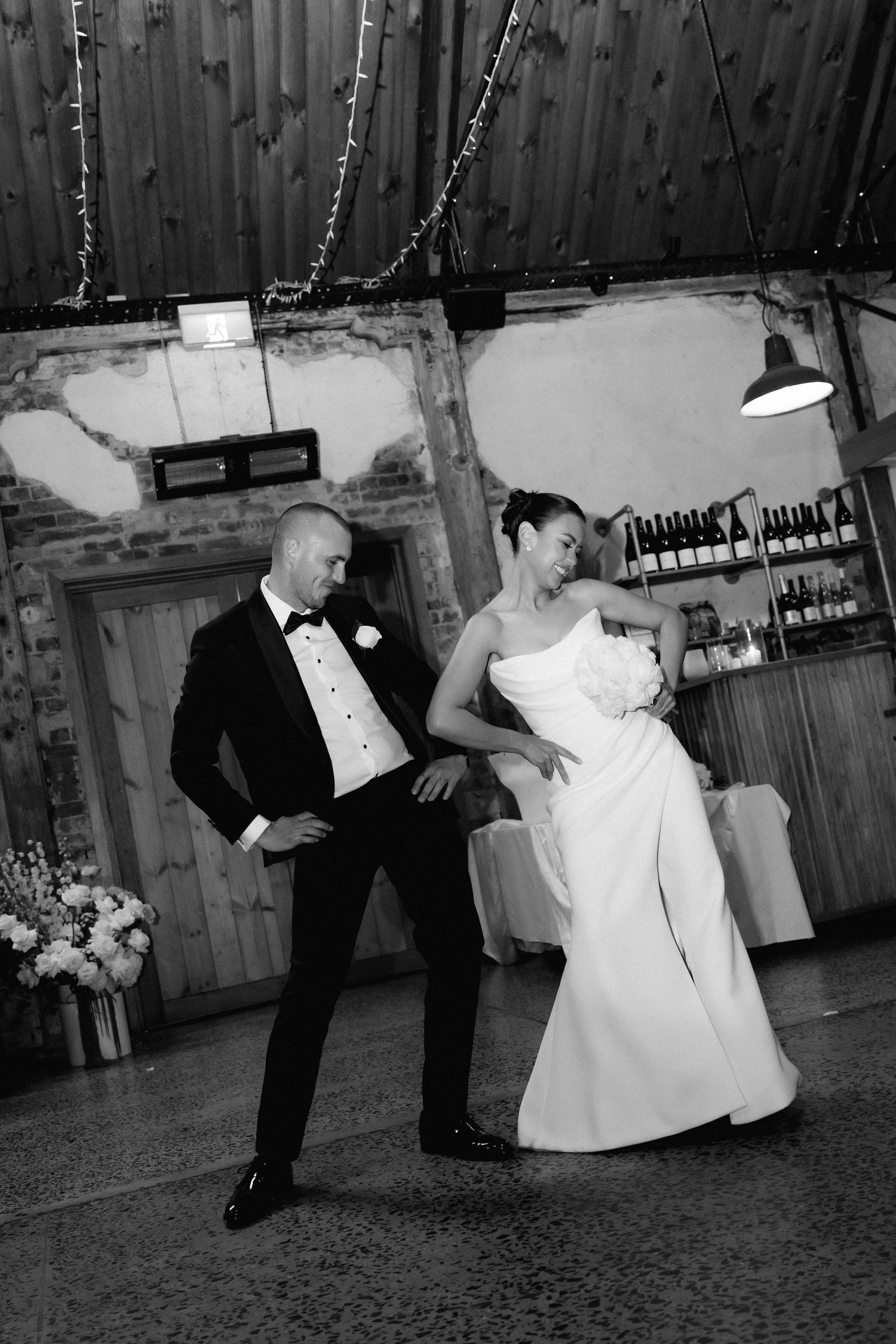 A series of black and white photos showing a couple dancing playfully in formal attire at a rustic venue.