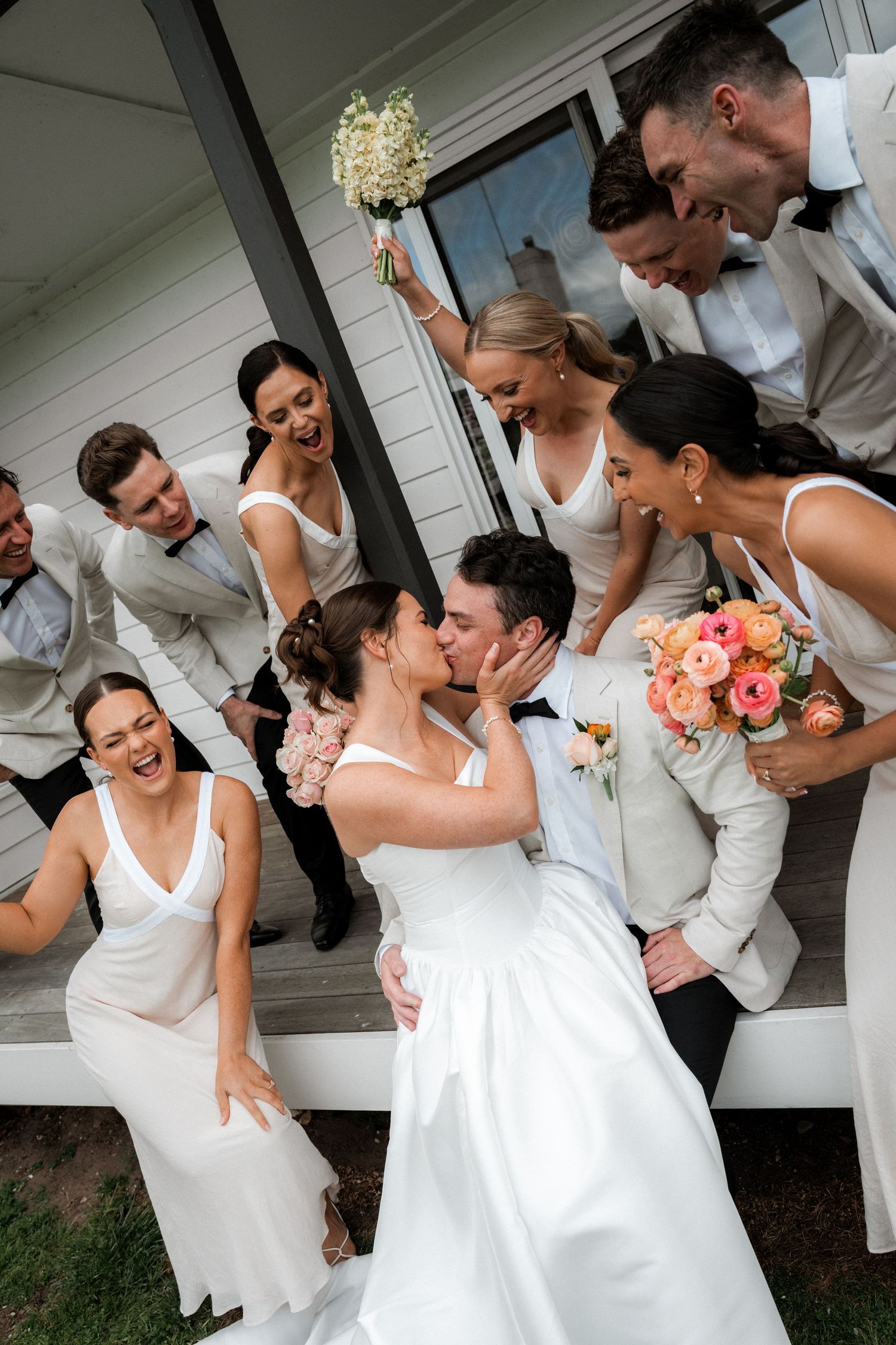 Wedding party shares laughter and candid moments on a white porch during celebration.