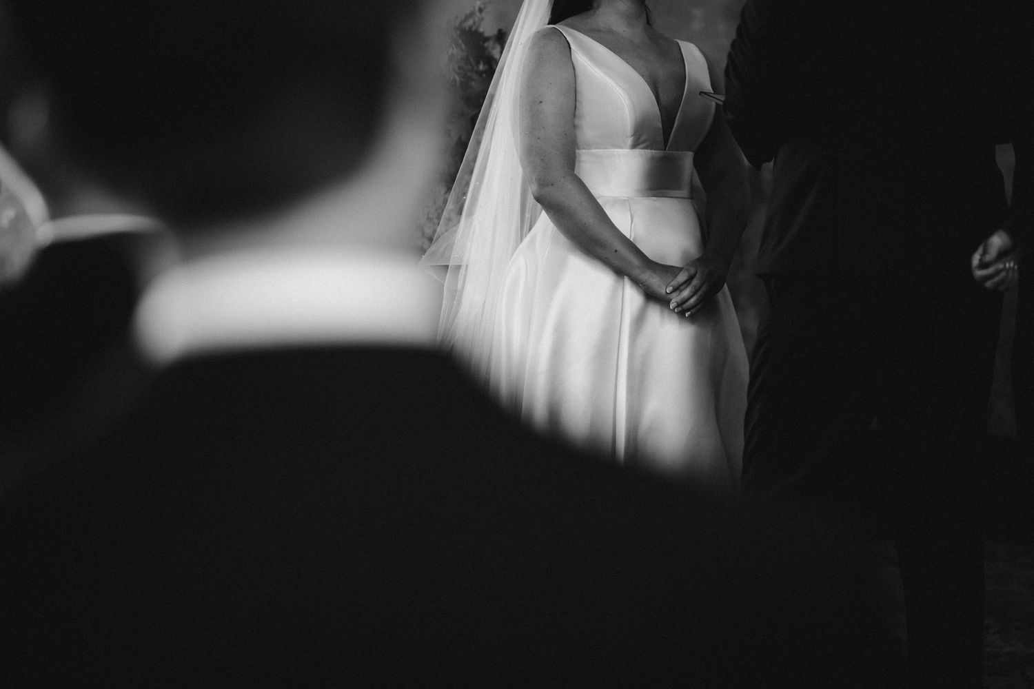 Close-up black and white detail of a bride's white wedding dress and gown shown in soft focus.