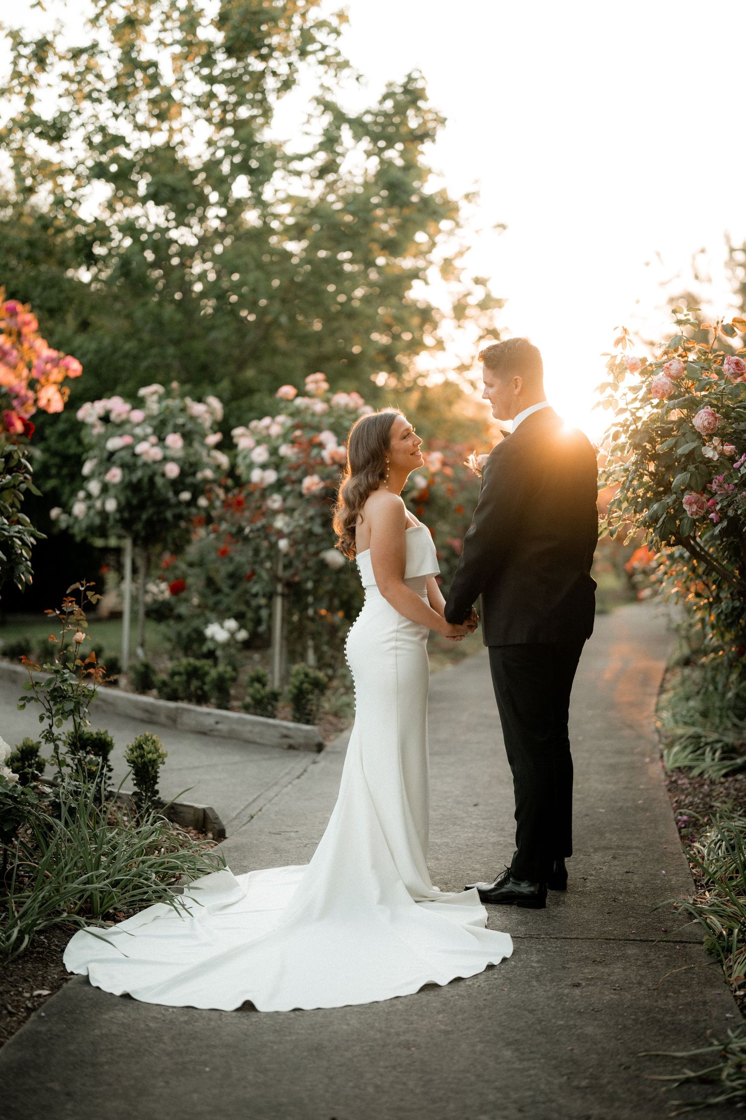 Romantic garden wedding photos with flowering roses and golden sunset light casting shadows on path.