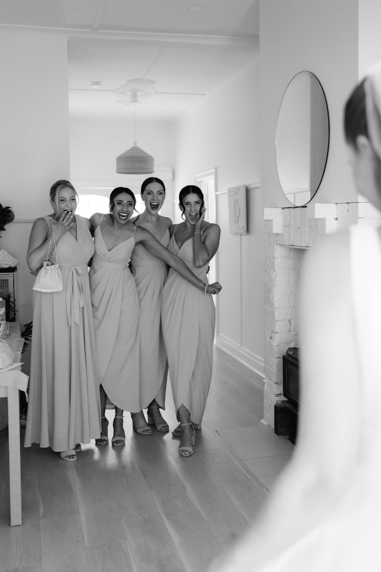 Group of bridesmaids in matching light gray dresses pose together in a bright white room.