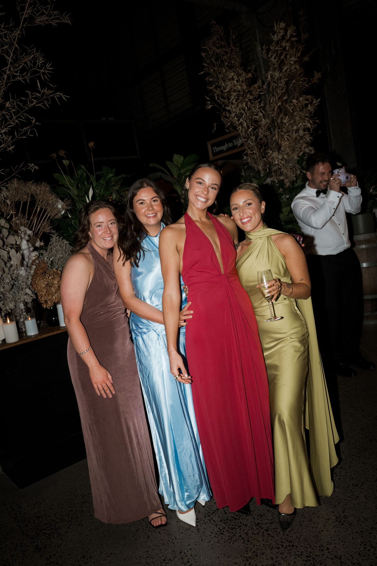 Four people in colorful formal dresses pose together at an outdoor evening event.