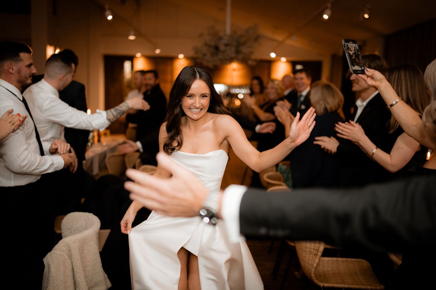 A joyful bride dances with guests during the wedding reception in a warmly lit venue.