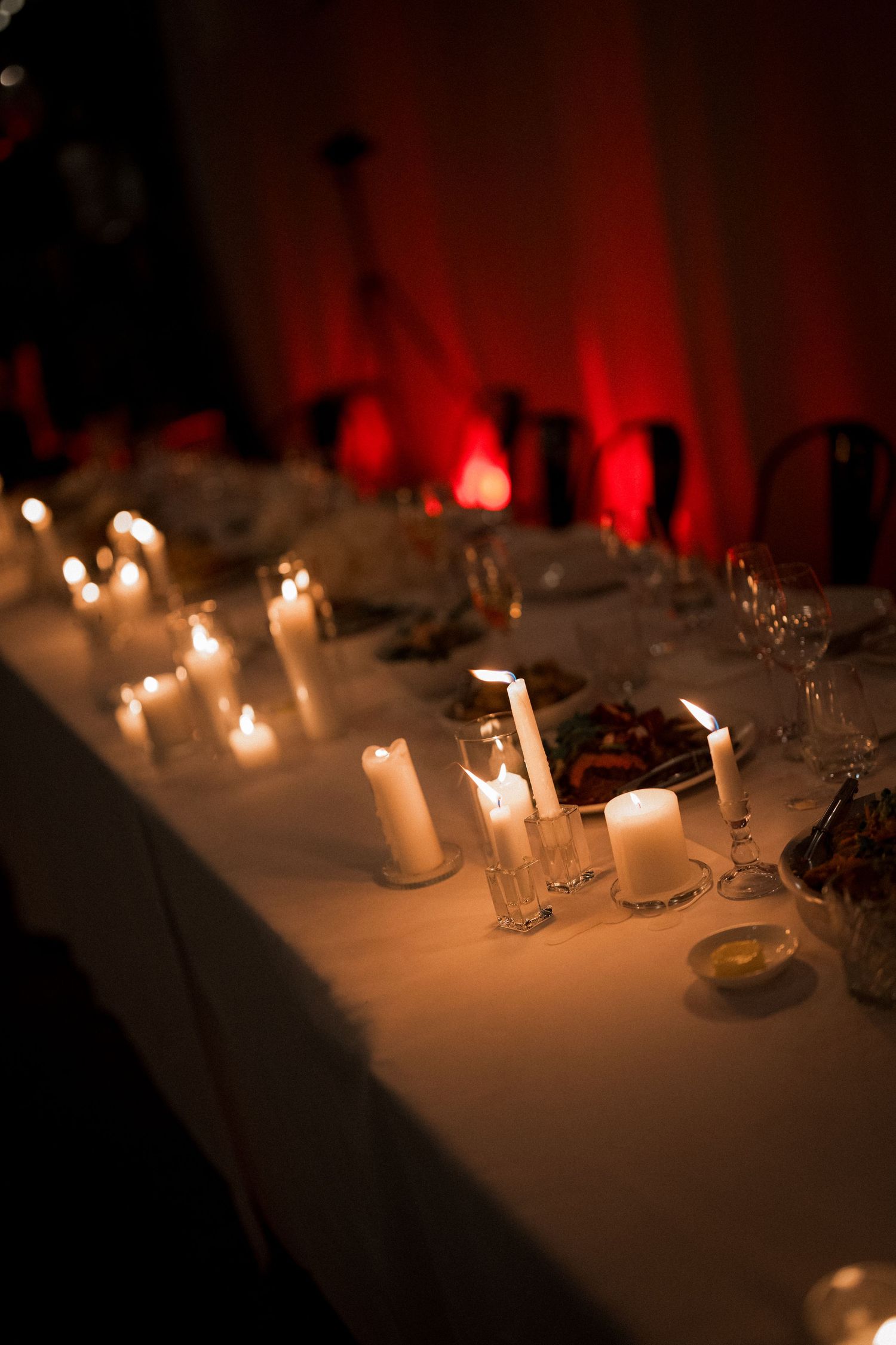 Candlelit wedding reception tables decorated with white linens and glowing red ambient lighting.