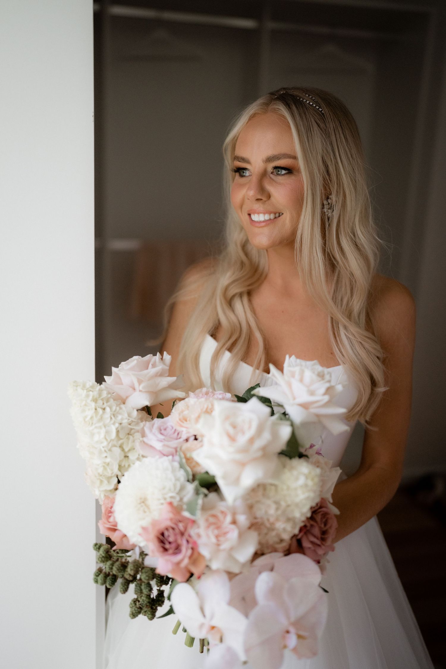 A beautiful bridal bouquet featuring soft pink roses and white hydrangeas against a dark background.