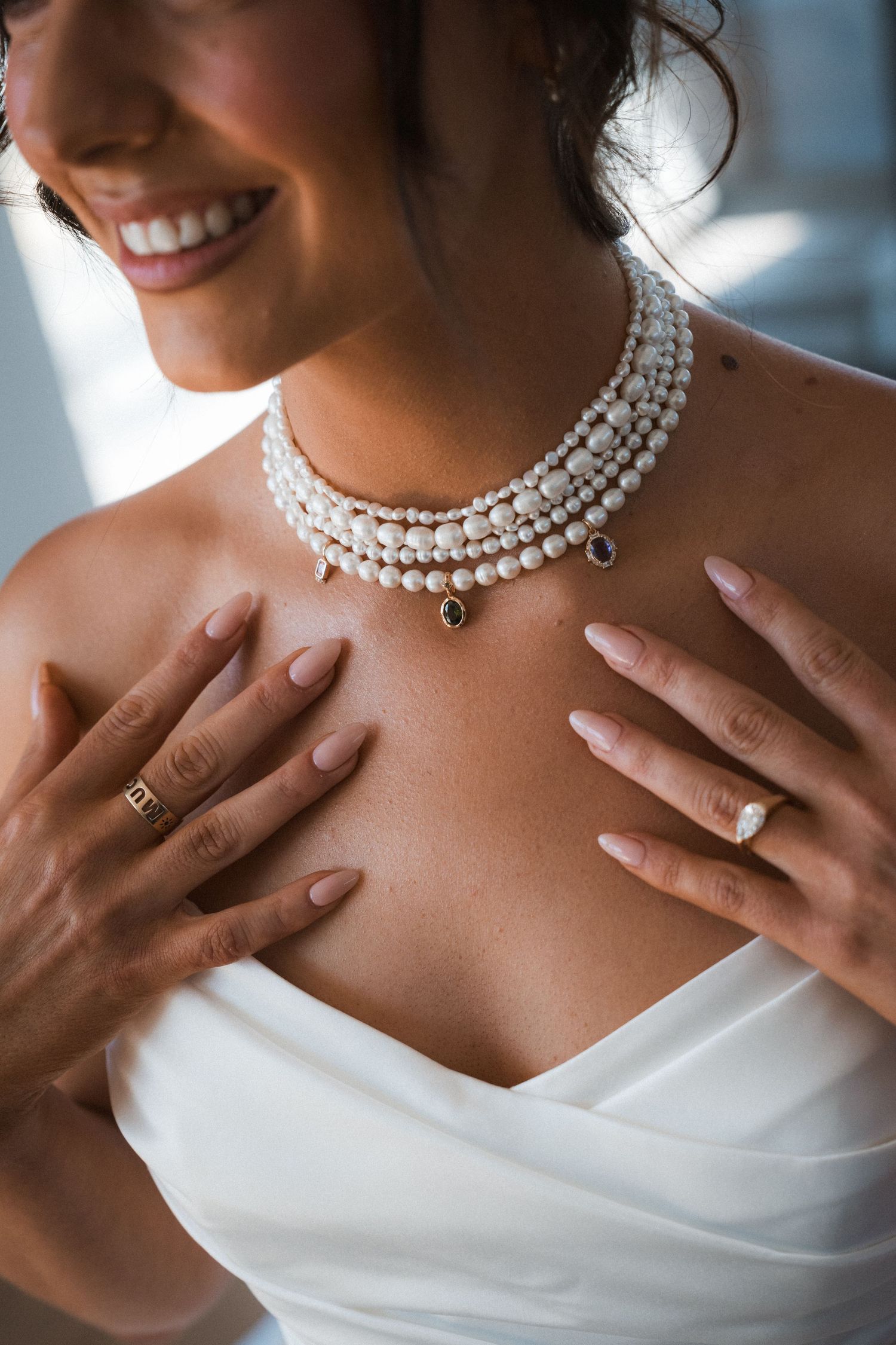 Close-up shots of an elegant pearl necklace and hands against a white wedding dress.