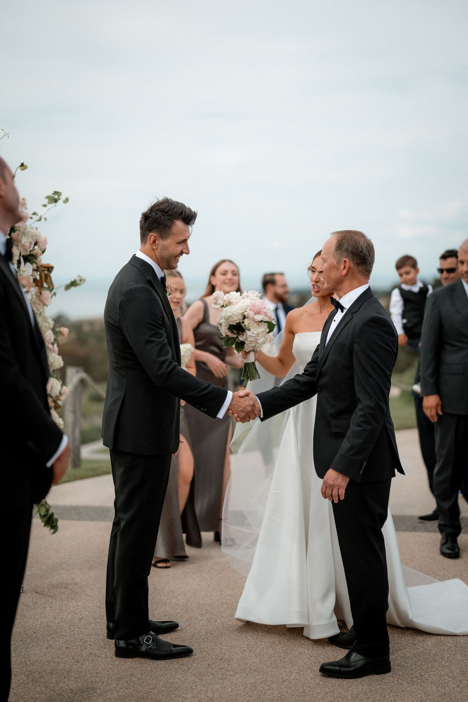 Wedding party members gather outdoors as guests congratulate and celebrate during the ceremony.
