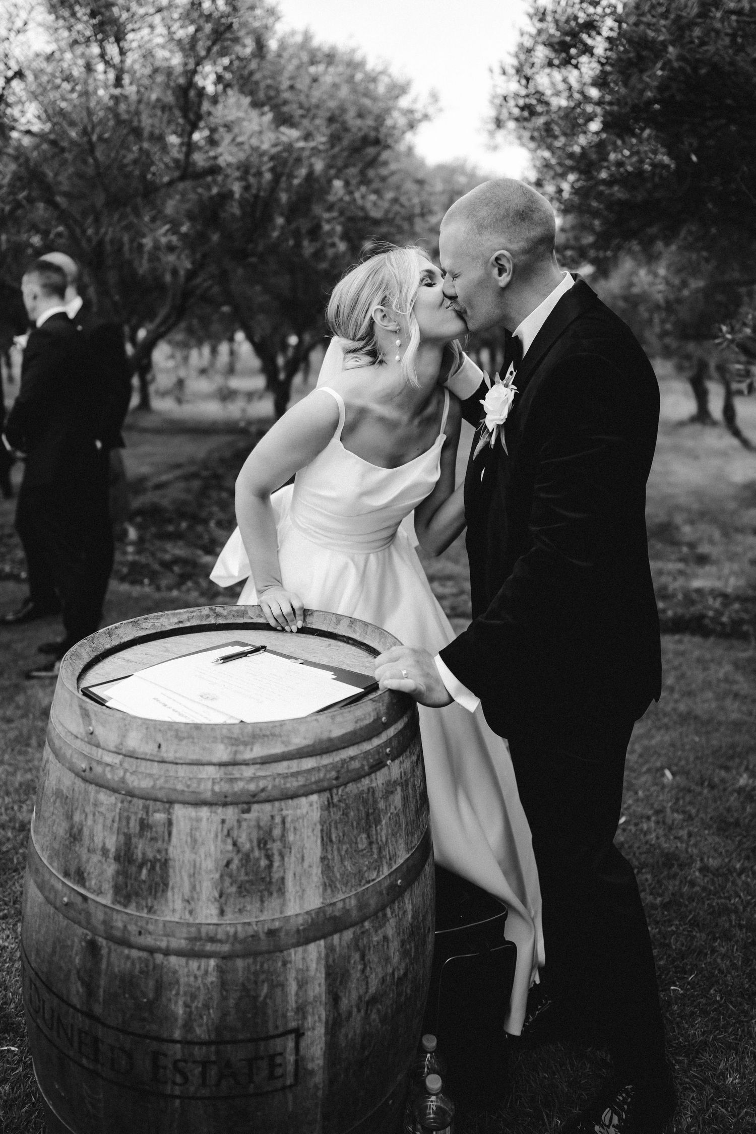 A series of black and white wedding photos featuring a couple posing playfully around rustic wine barrels.