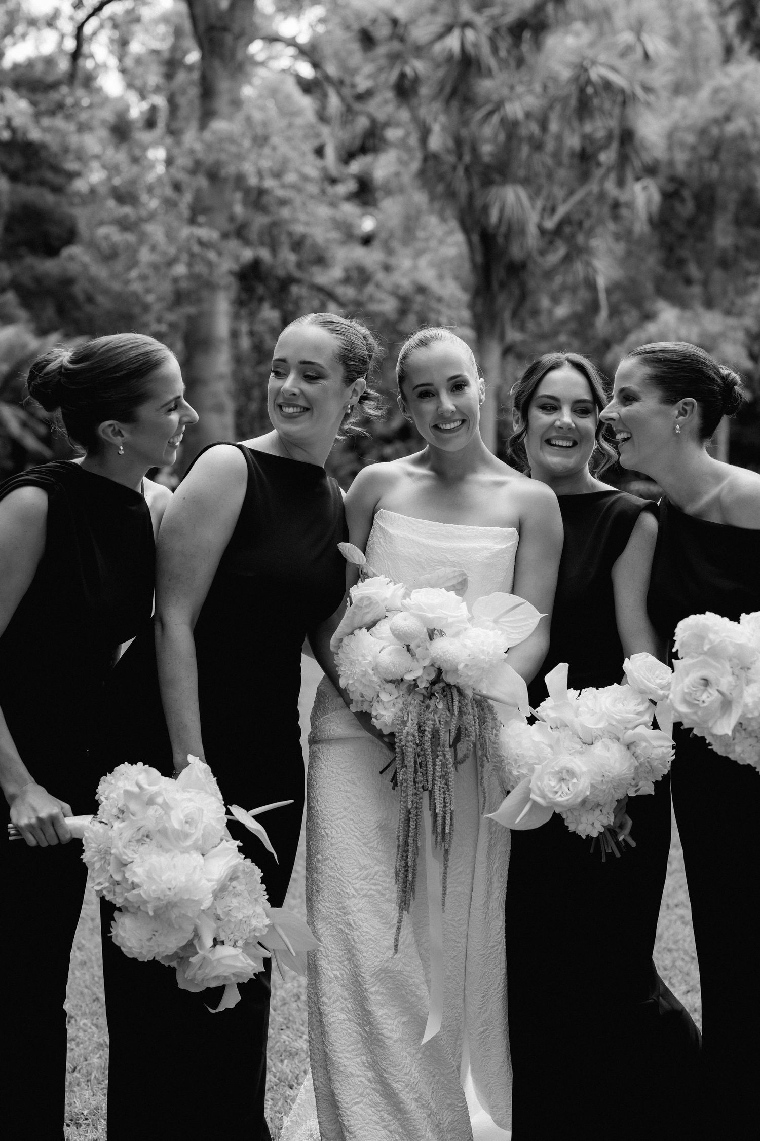 Black and white photo of bride in white gown surrounded by bridesmaids in black dresses.