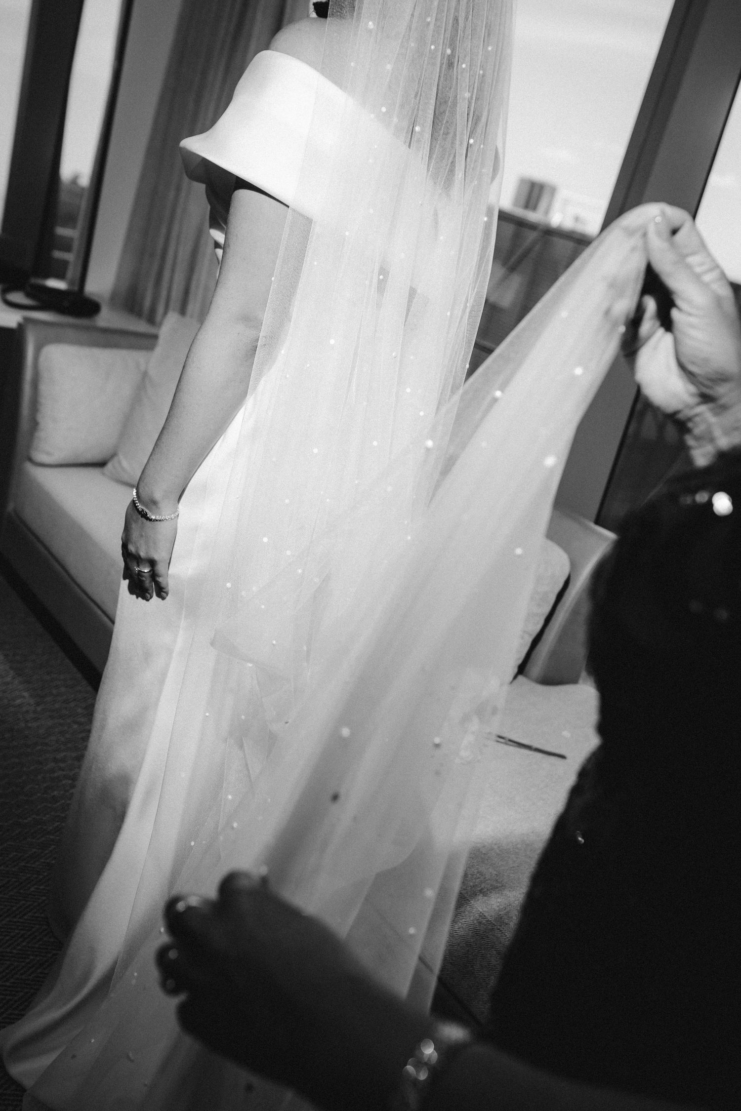 A close-up black and white photo of a wedding veil being adjusted, showing delicate details and fabric movement.