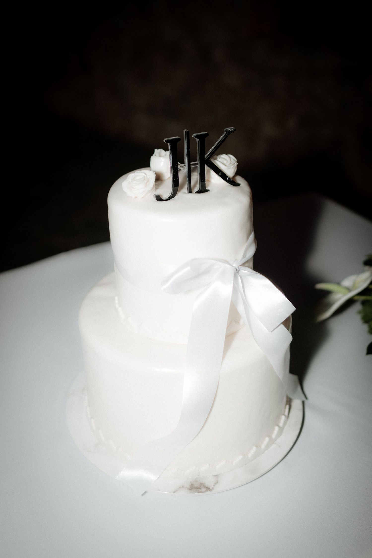 Elegant white two-tier wedding cake with JK monogram topper and bow detail.