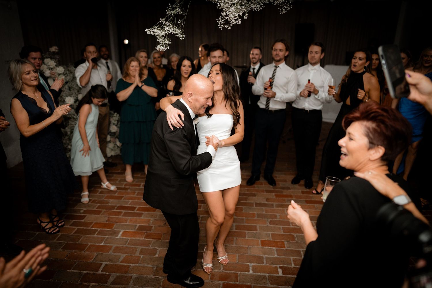 Wedding guests dance and celebrate on a rustic brick dance floor under twinkling lights.