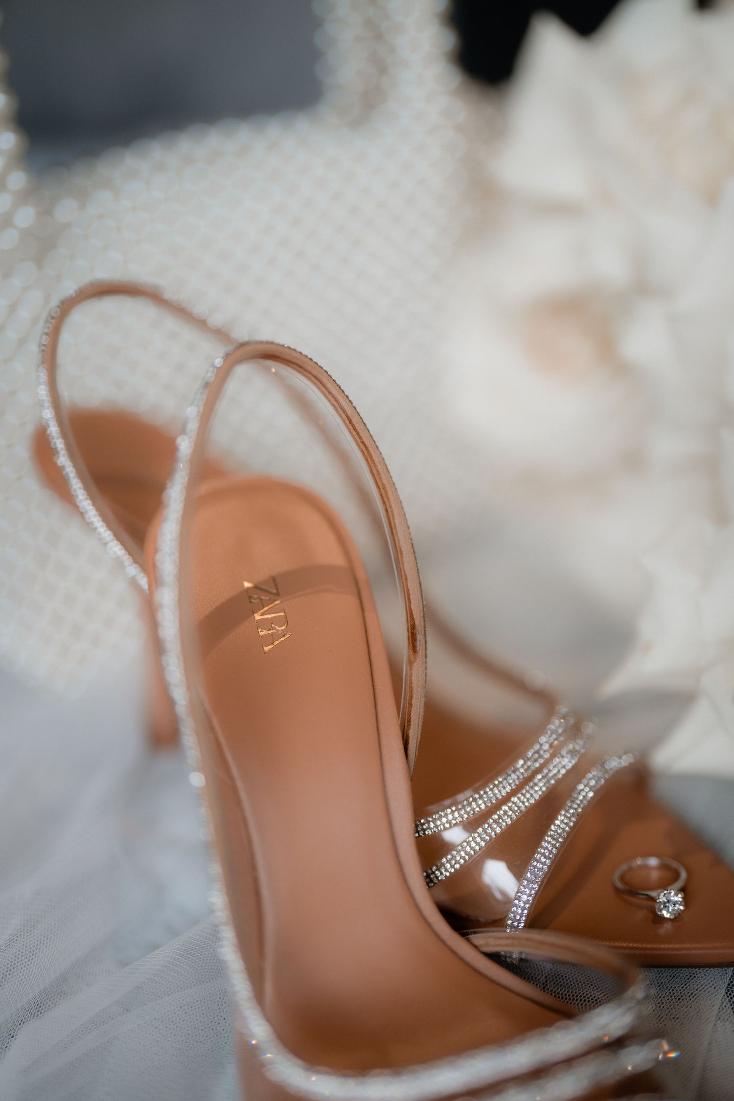 Elegant crystal-embellished bridal slingback heel with rhinestone straps displayed against white tulle fabric.