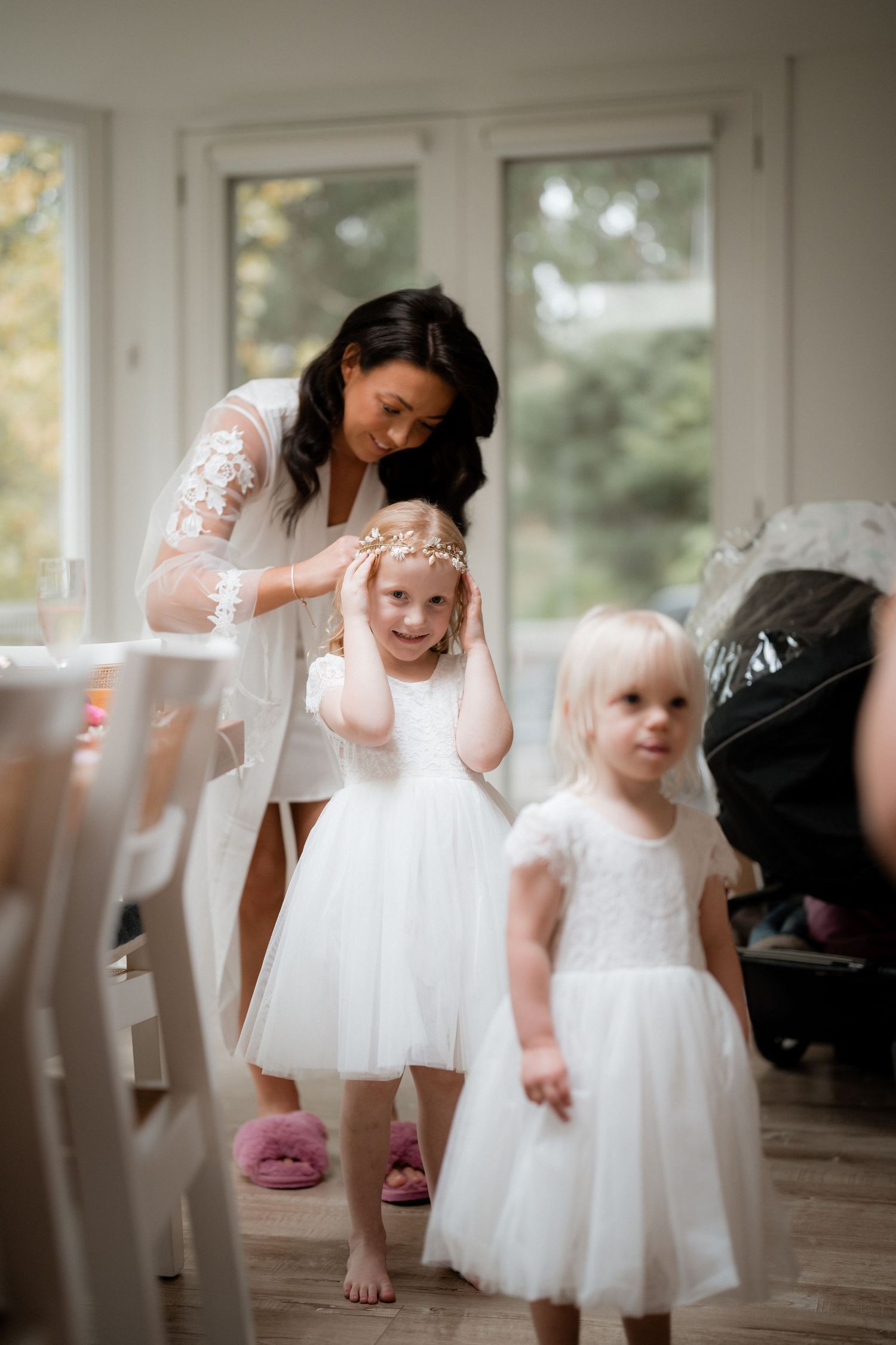 Two children in white tulle dresses stand with a woman in white lace during an indoor celebration.