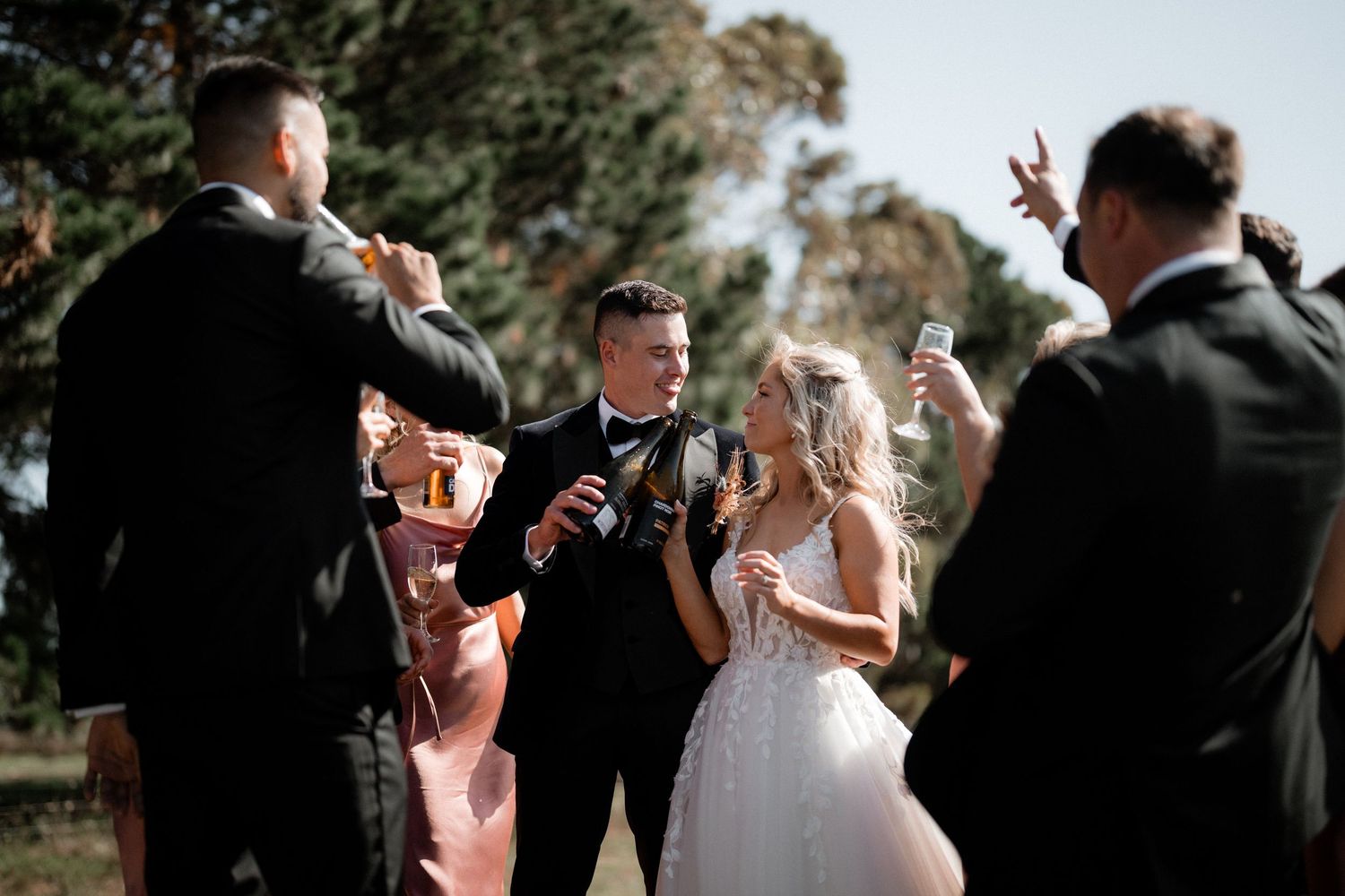 Wedding party enjoys champagne toasts during an outdoor celebration on a sunny day.