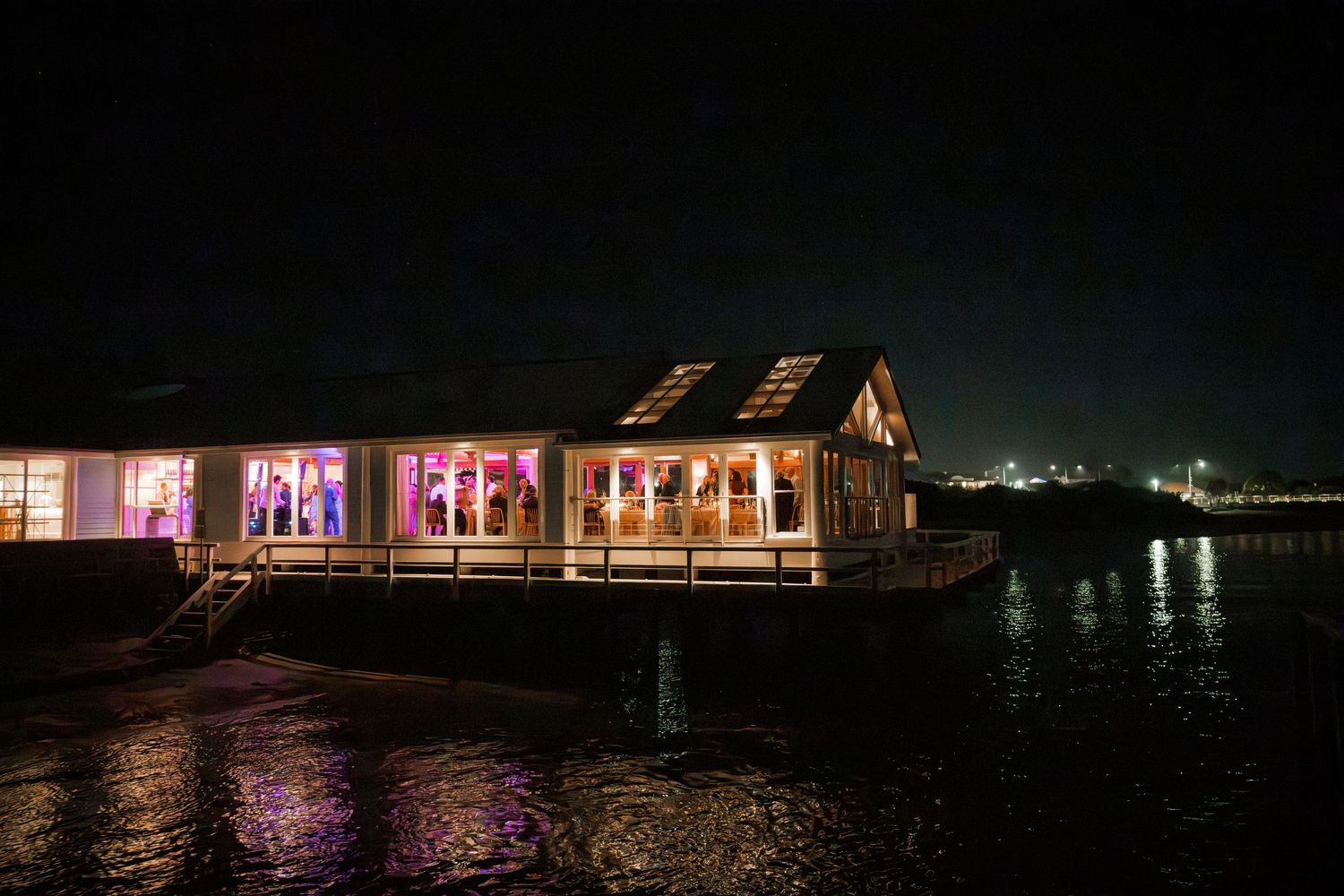 Wedding venue lit up at night with purple lighting reflecting on water.