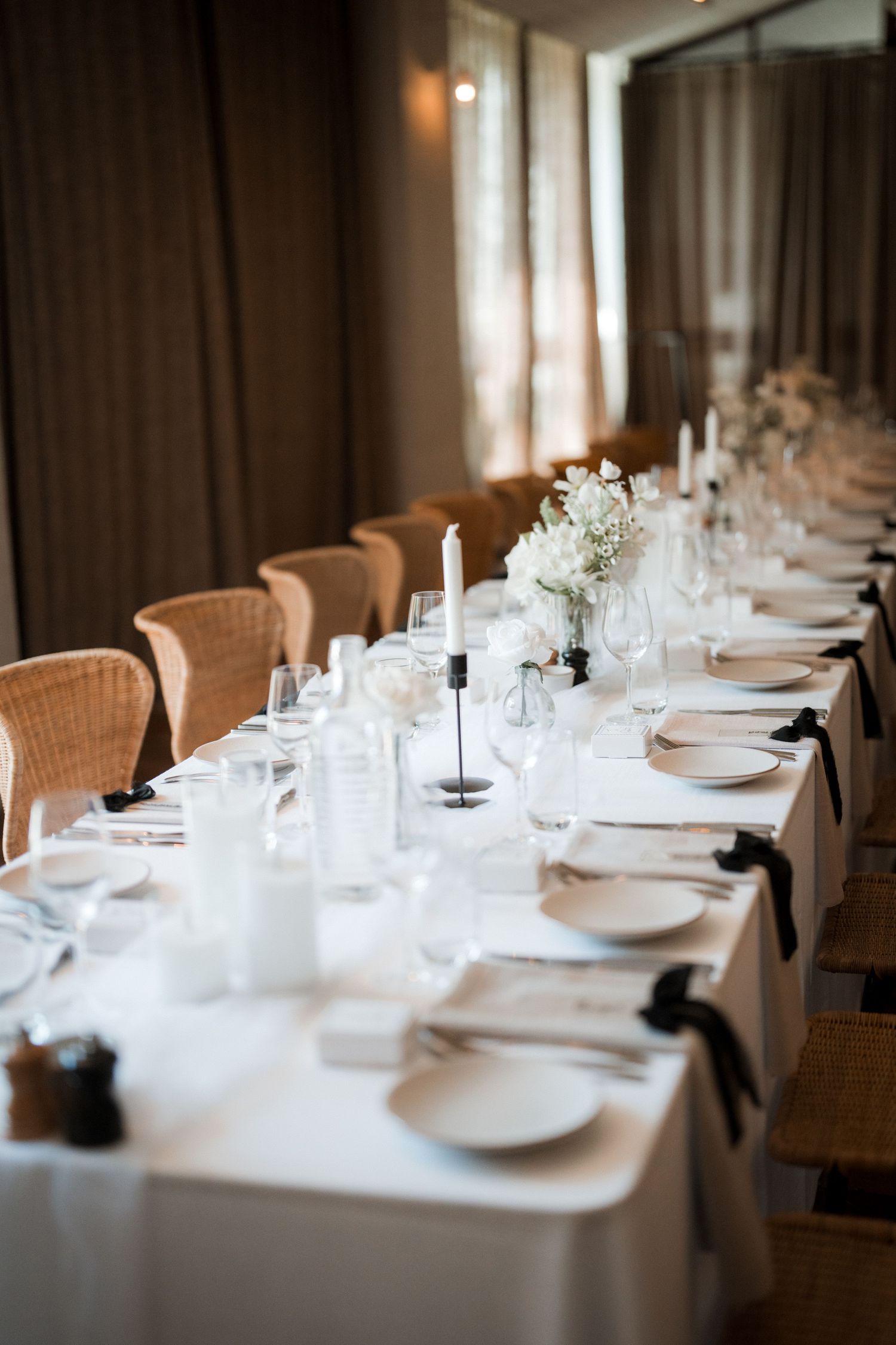 Minimalist wedding table decor featuring white tablecloths and wicker chairs in a warm, intimate setting.