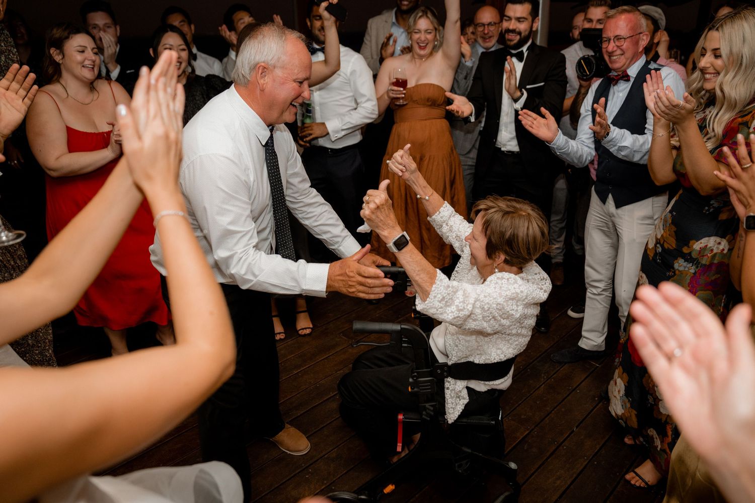 Lively wedding reception crowd dancing and celebrating with hands raised in the air.