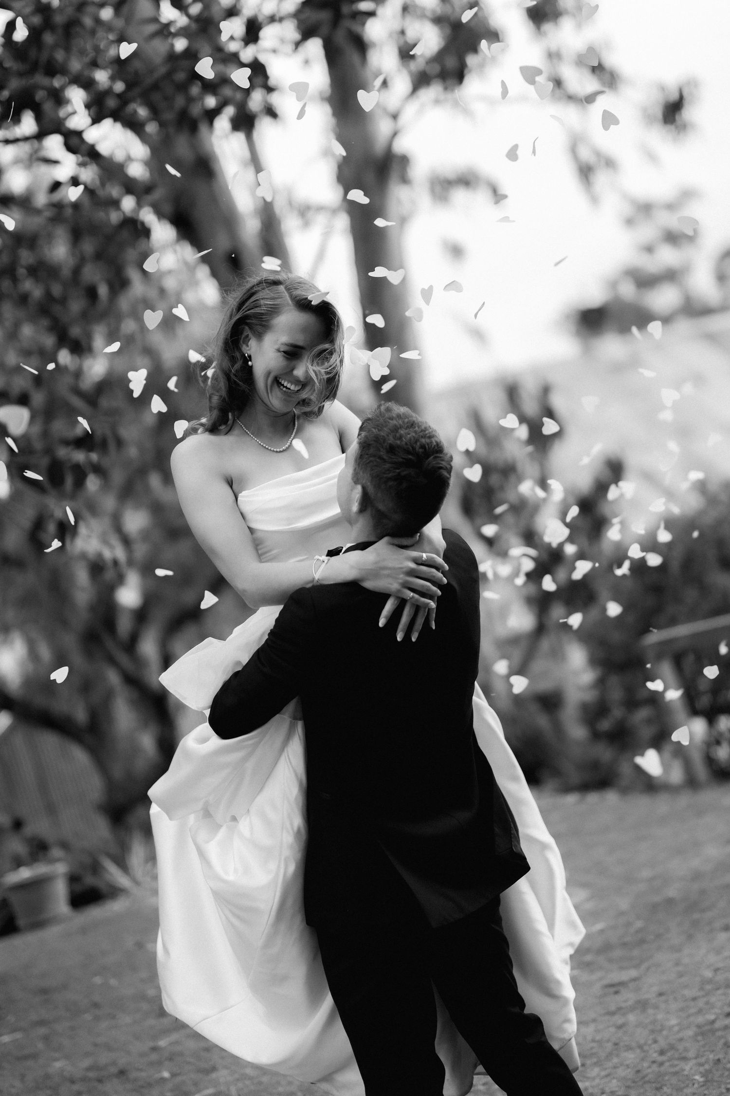 Wedding couple dancing playfully outdoors with confetti falling around them.