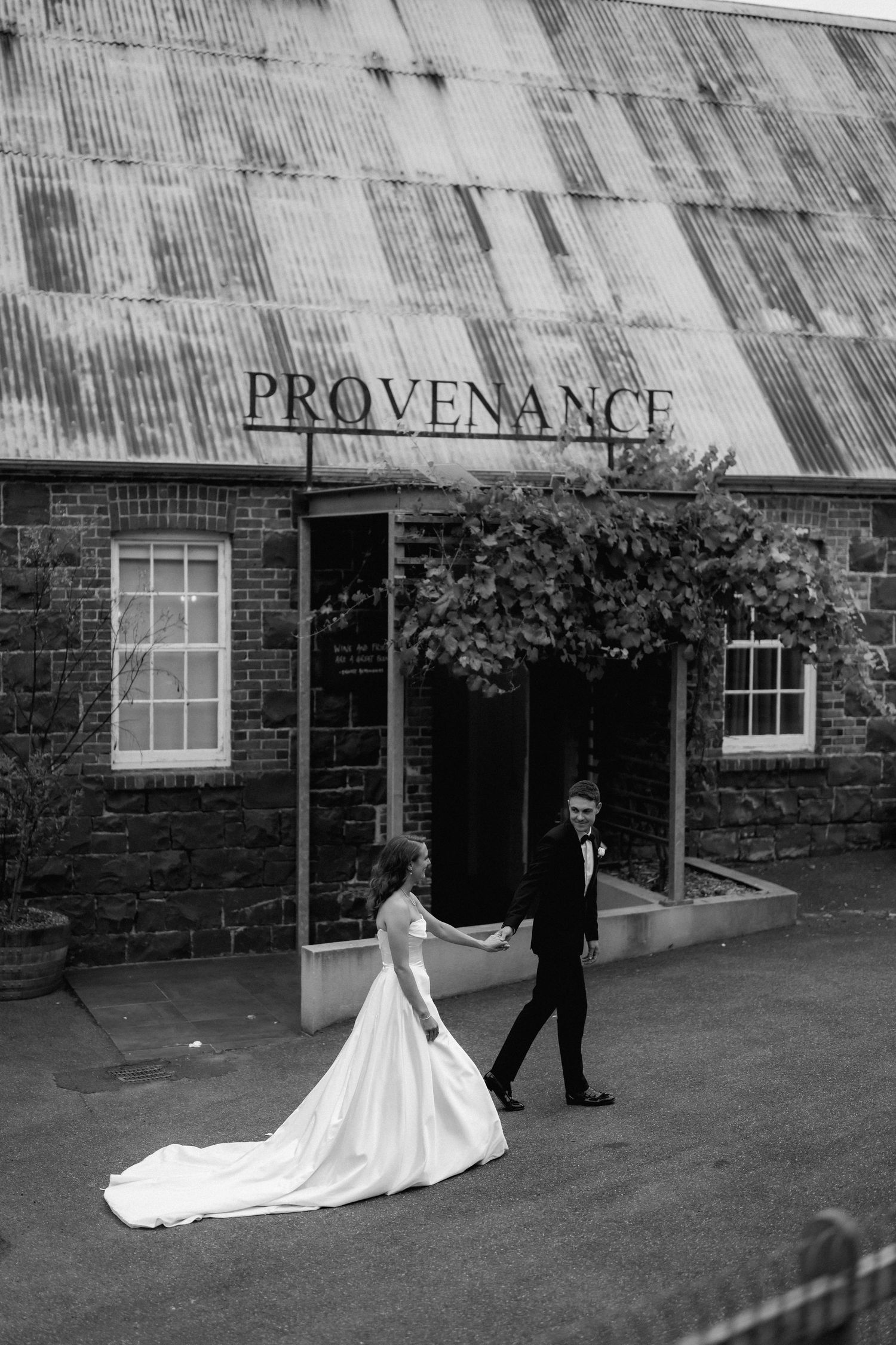 Wedding couple poses in front of rustic building with 'Provenance' signage.