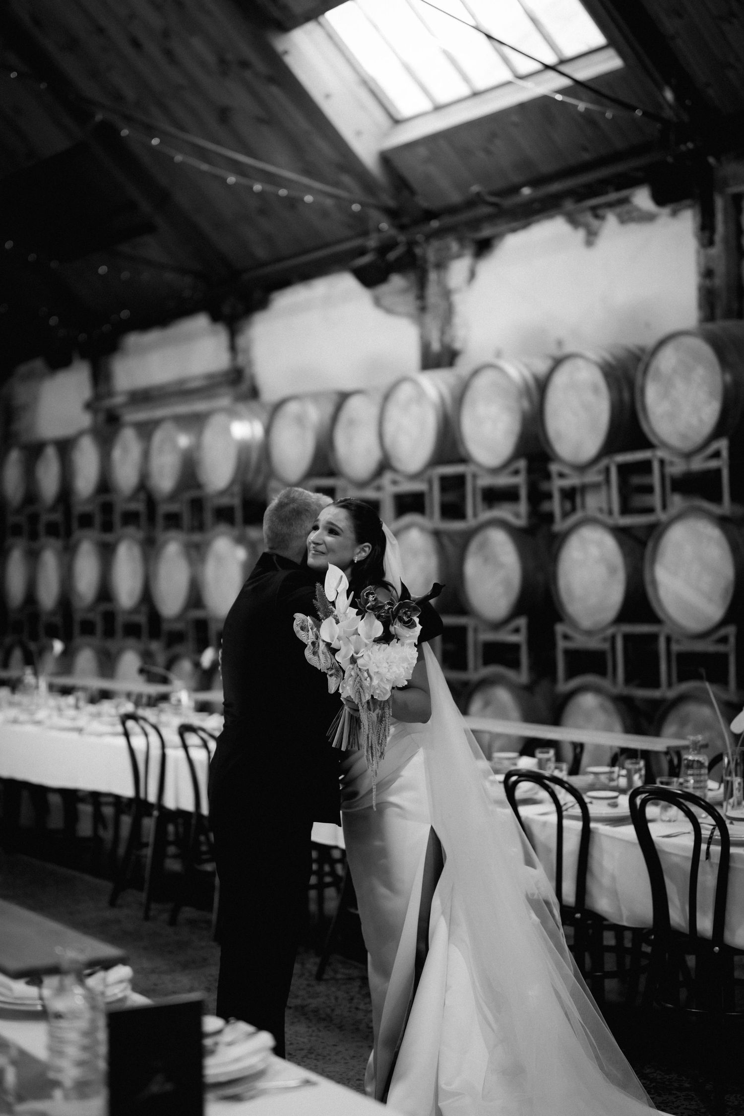 Black and white wedding photos showing a couple dancing in a rustic venue with wine barrels in the background.